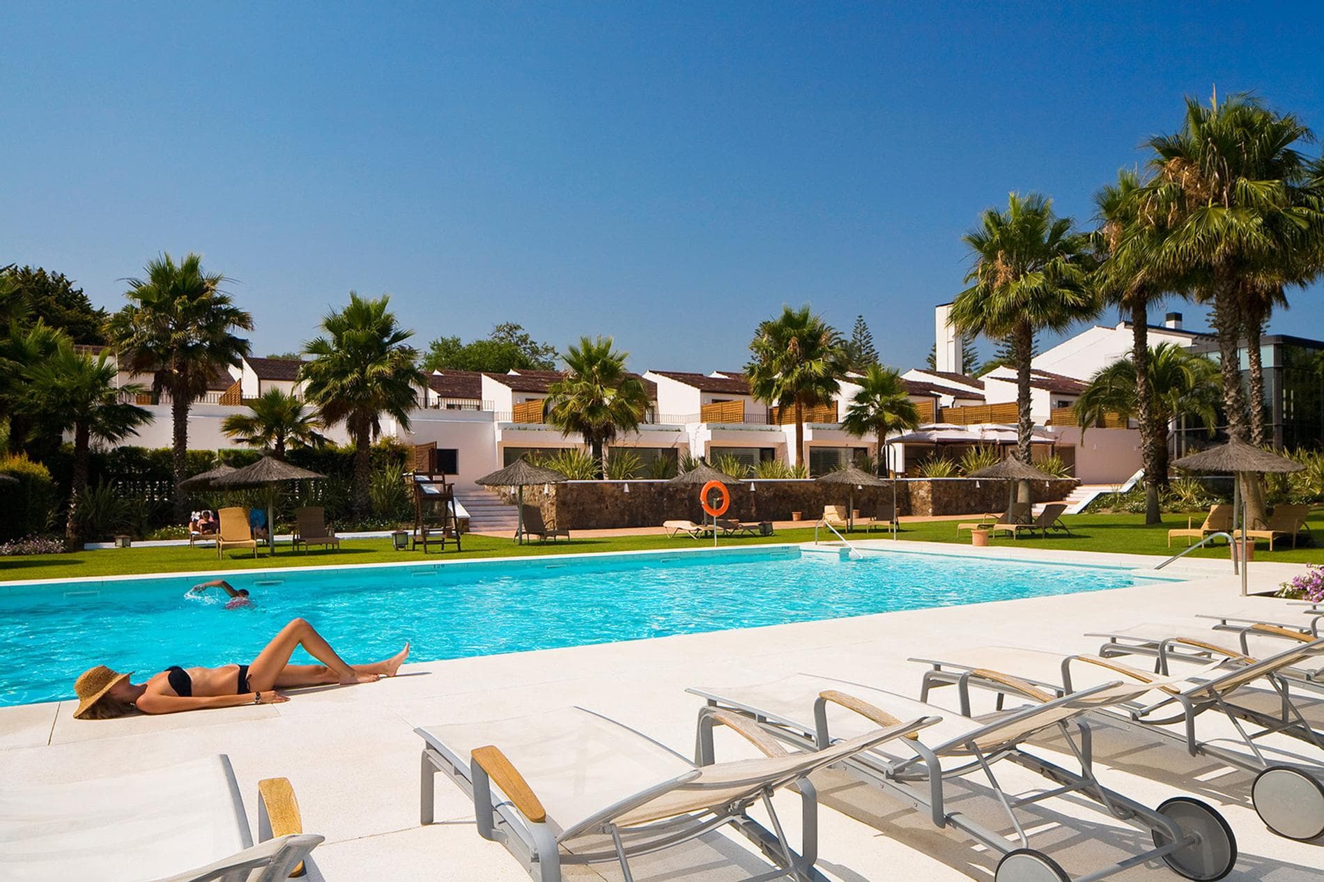 An outdoor swimming pool surrounded by sunbeds under clear blue skies