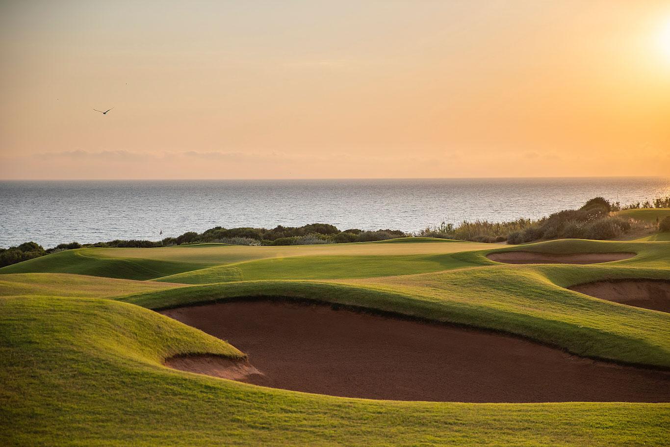 Undulating fairway interspersed with bunkers with the sea in the background, at sunset