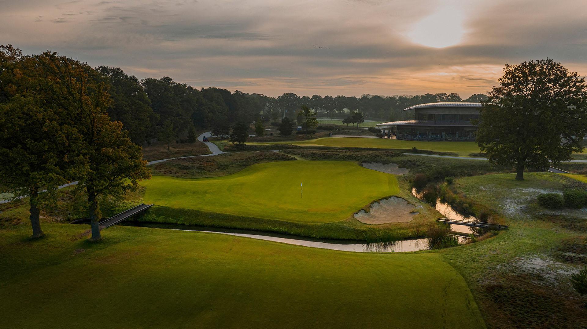 Overhead view of a smooth green surrounded by a water feature with a bridge to navigate the course at sun set