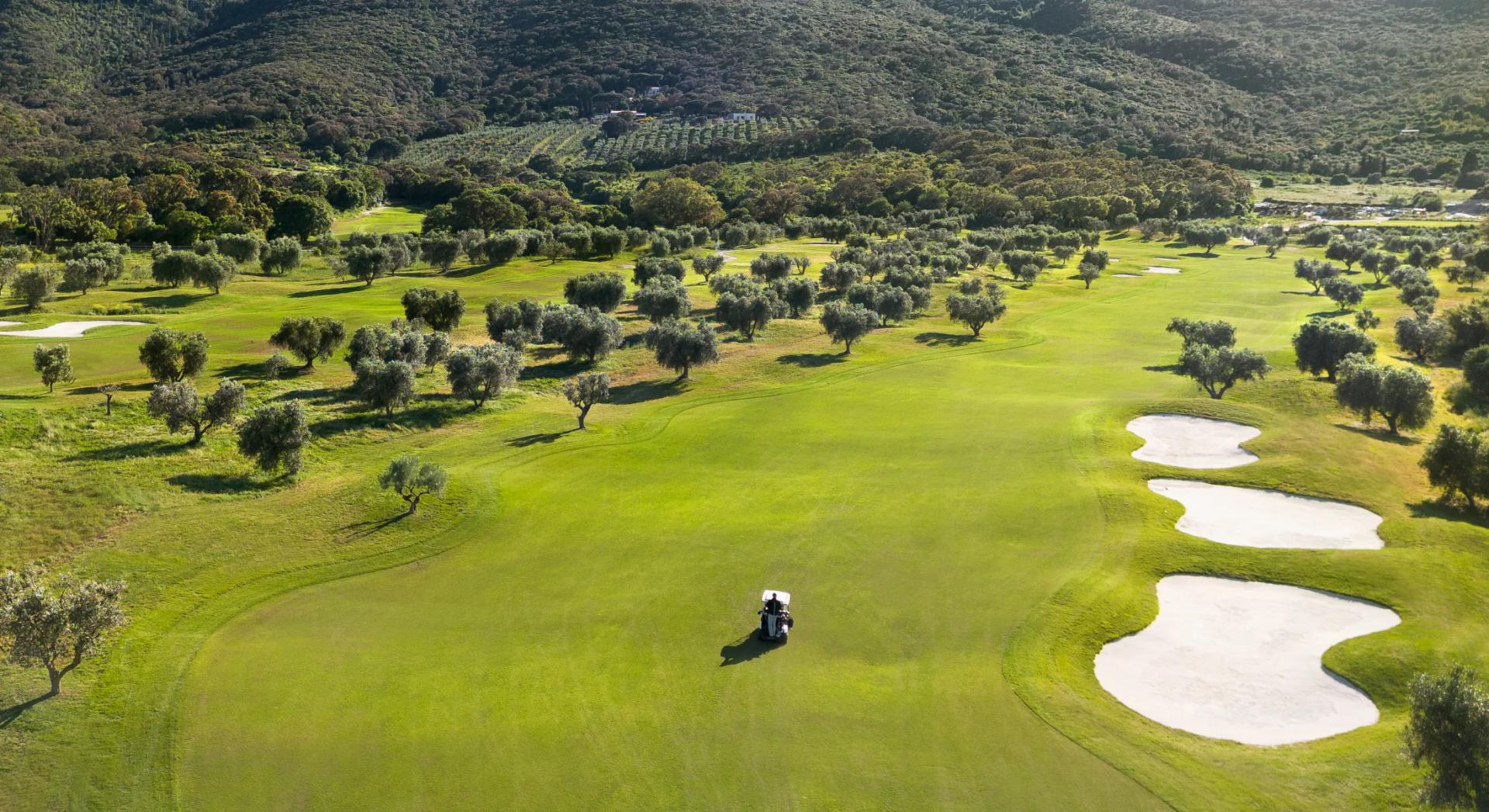A wide fairway nestled with sand bunkers with a buggy driving down the centre
