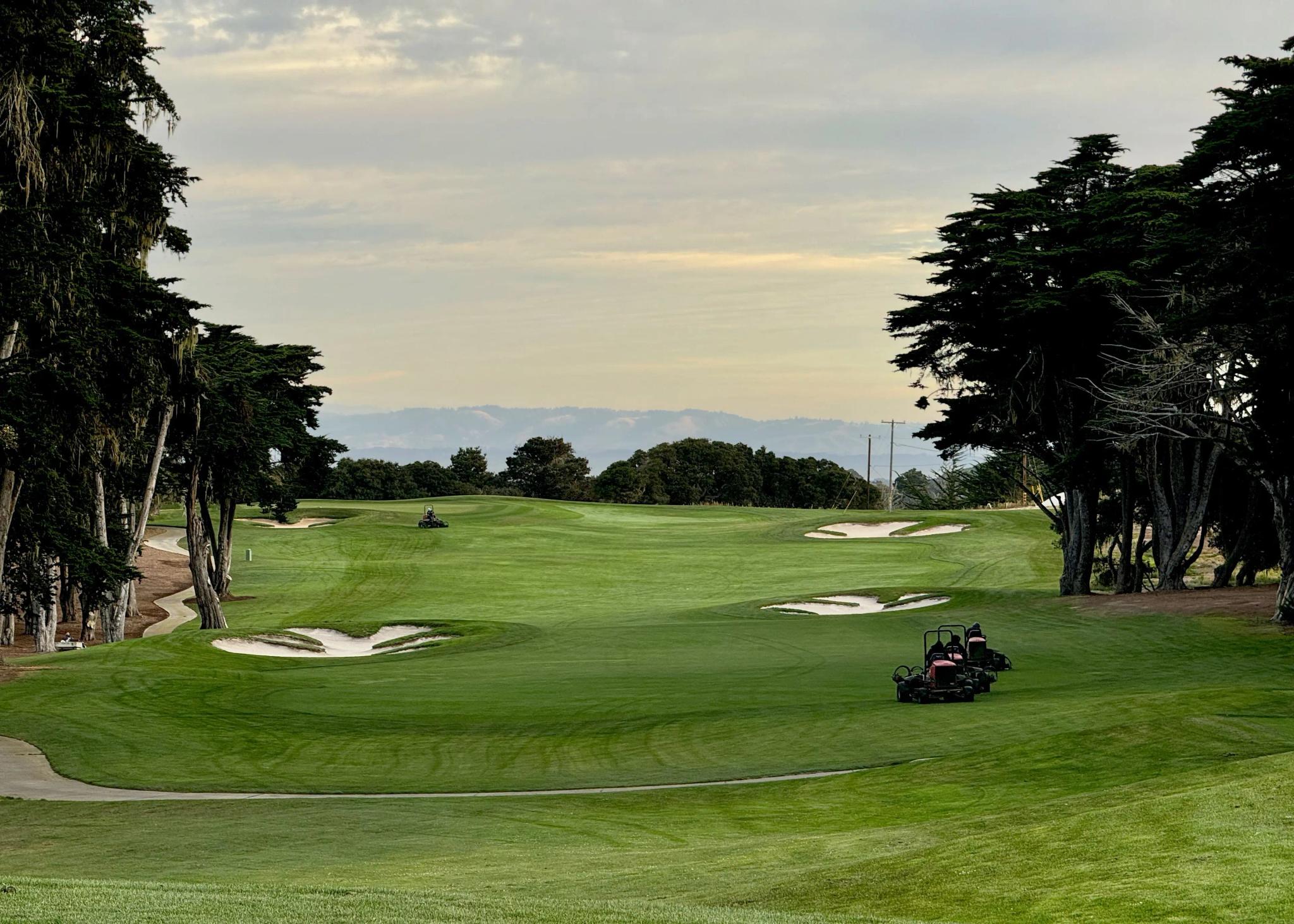 A wide fairway nestled with sand bunkers with mountain views in the distance
