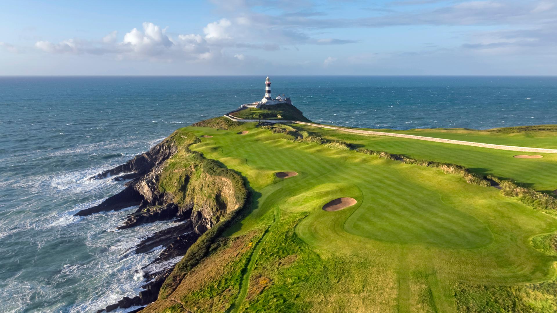 Aerial view of a fairway nestled with sand bunkers with a lighthouse on the edge of the cliff