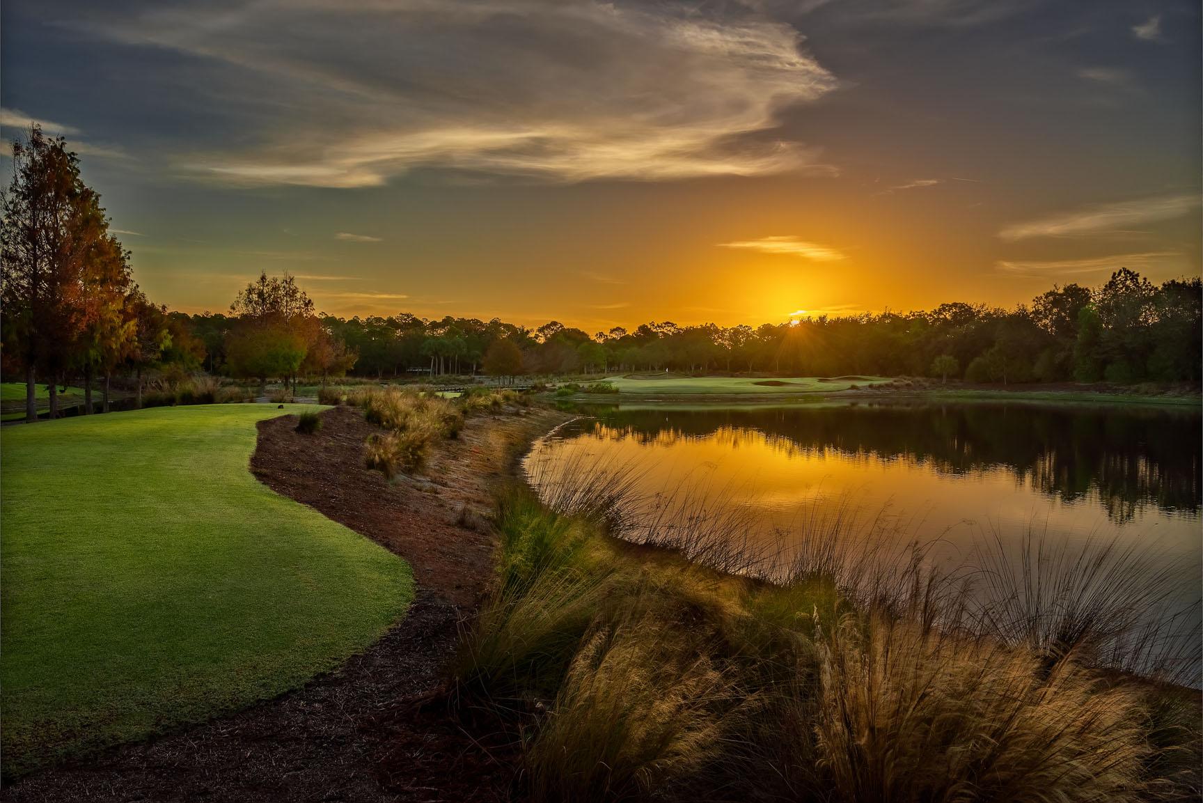 A stunning golf course at sunset with golden light reflecting off a calm lake.