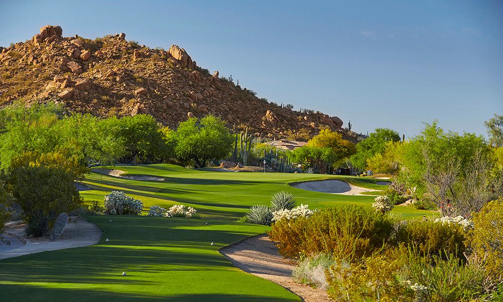 Rocky mountain towering over a green surrounded by sand bunkers