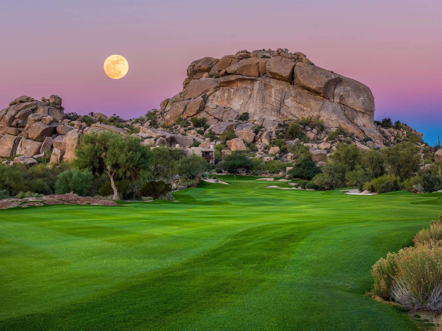 Moon glistening over a wide fairway leading to a manicured green in front of a mountain