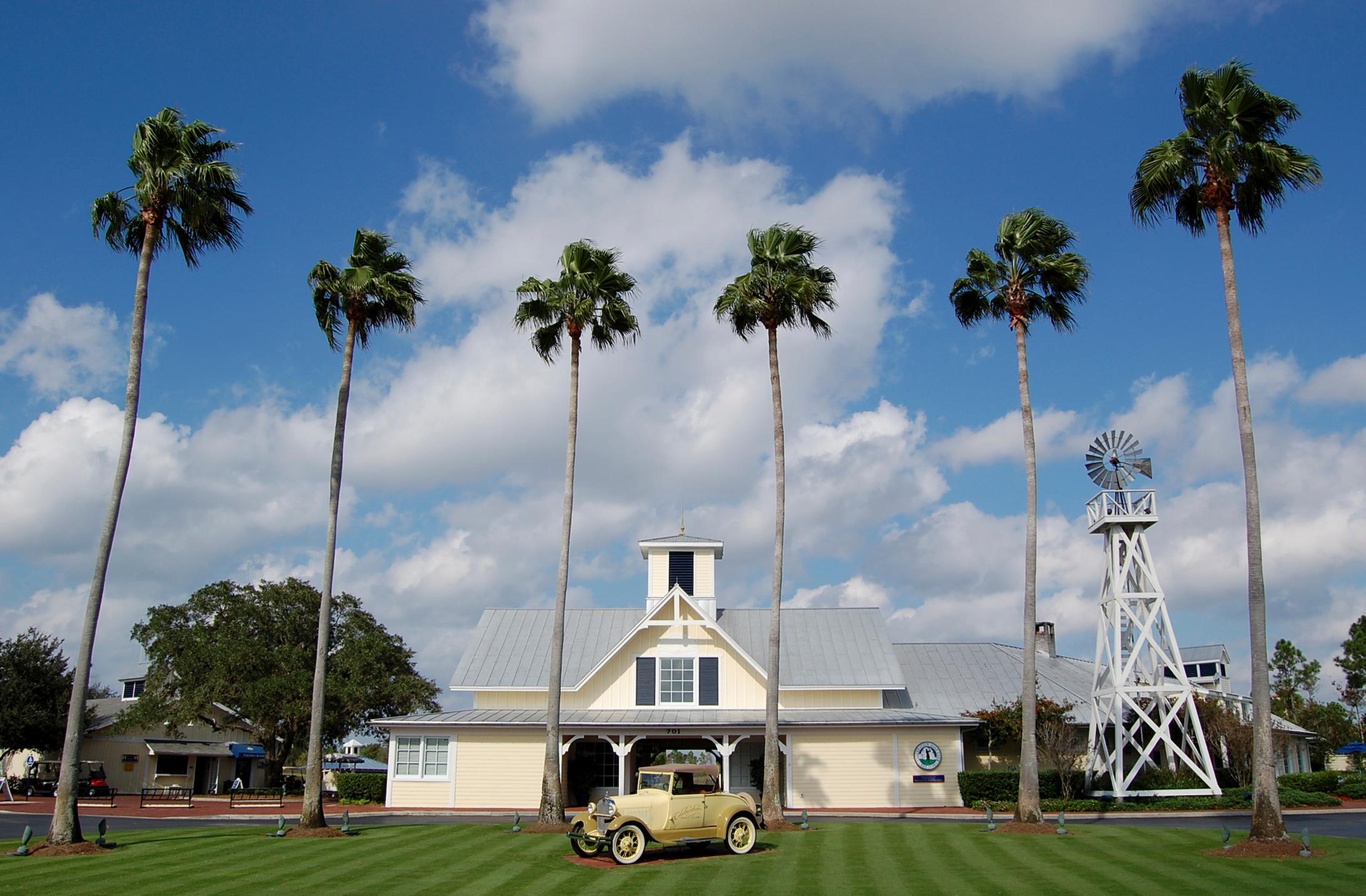 Palm trees surround a historic car placed as art work in front of the clubhouse