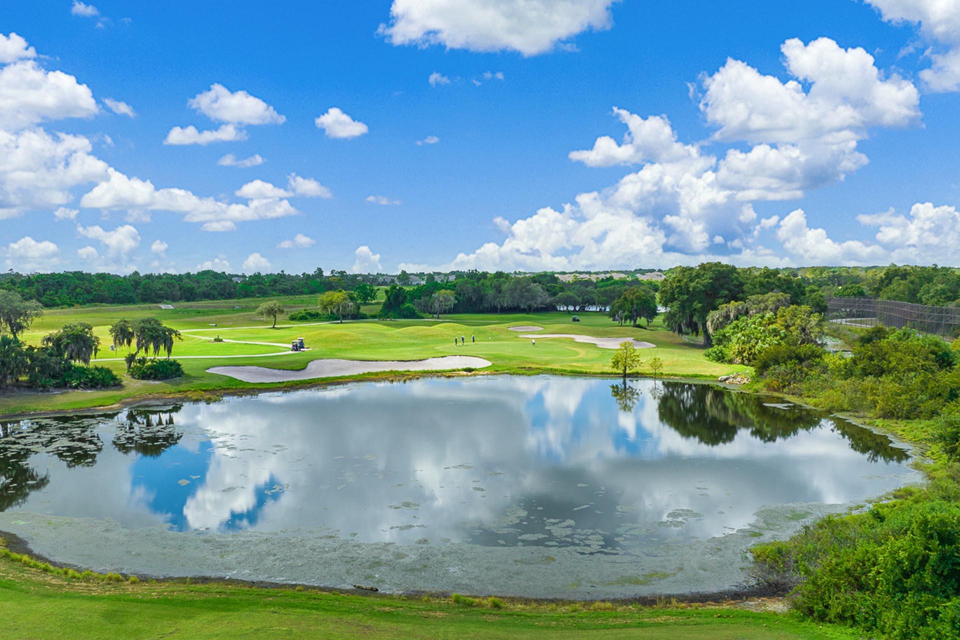 Aerial view of golfers enjoying their round on the green next to a large water hazard under blue skies