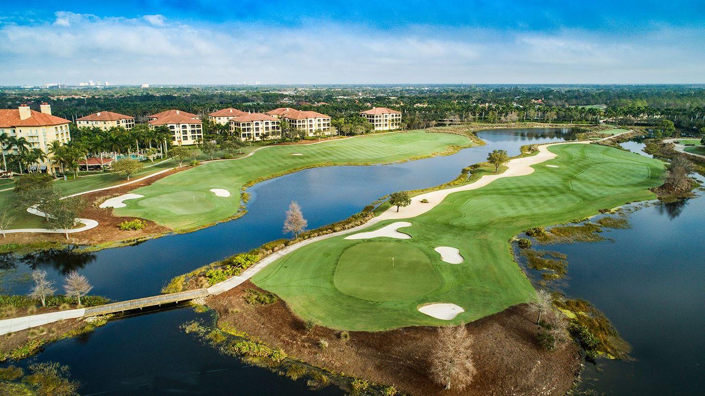A scenic golf course with winding fairways surrounded by calm blue water and luxury villas.