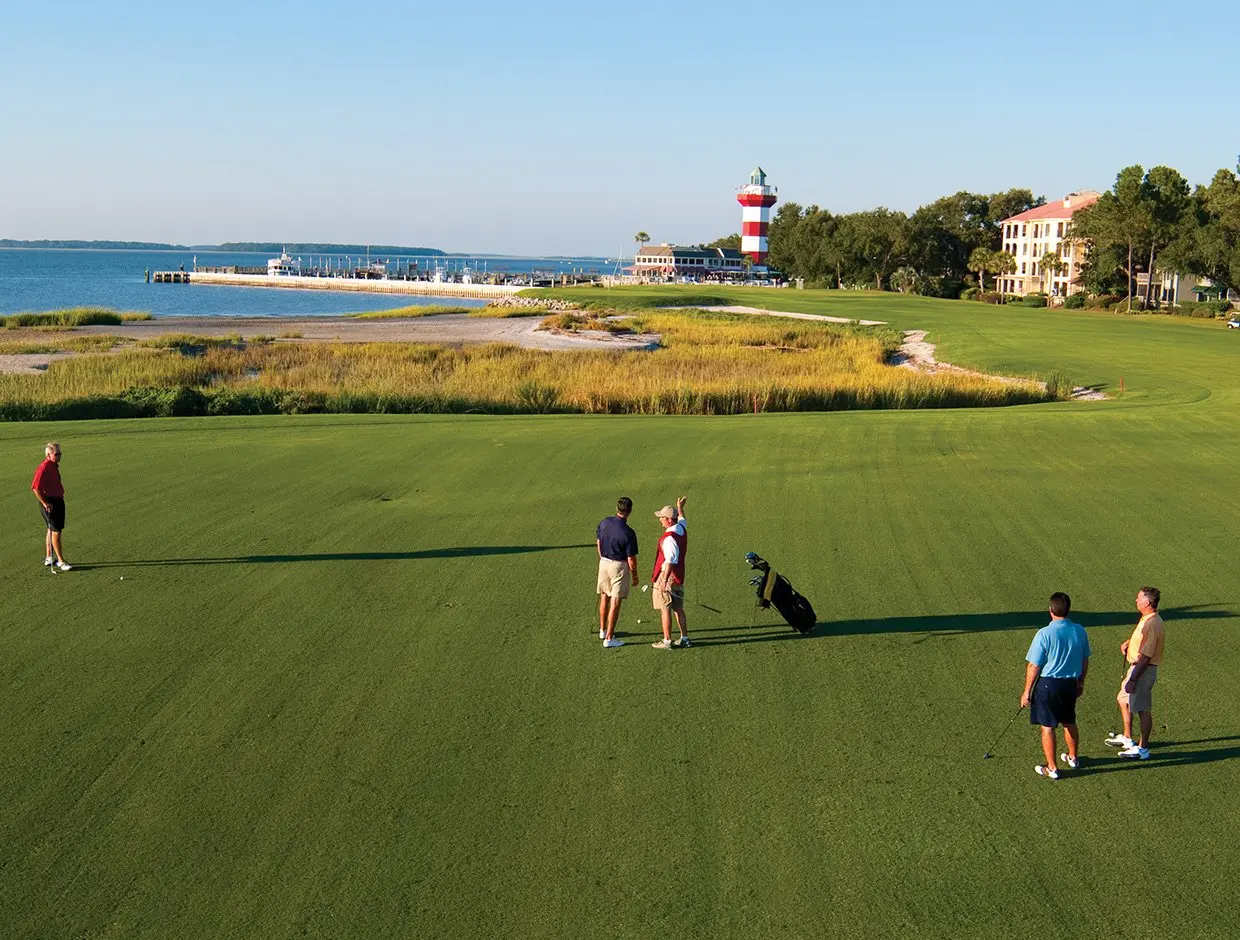 A group of golfers on a lush green fairway overlooking the harbor.
