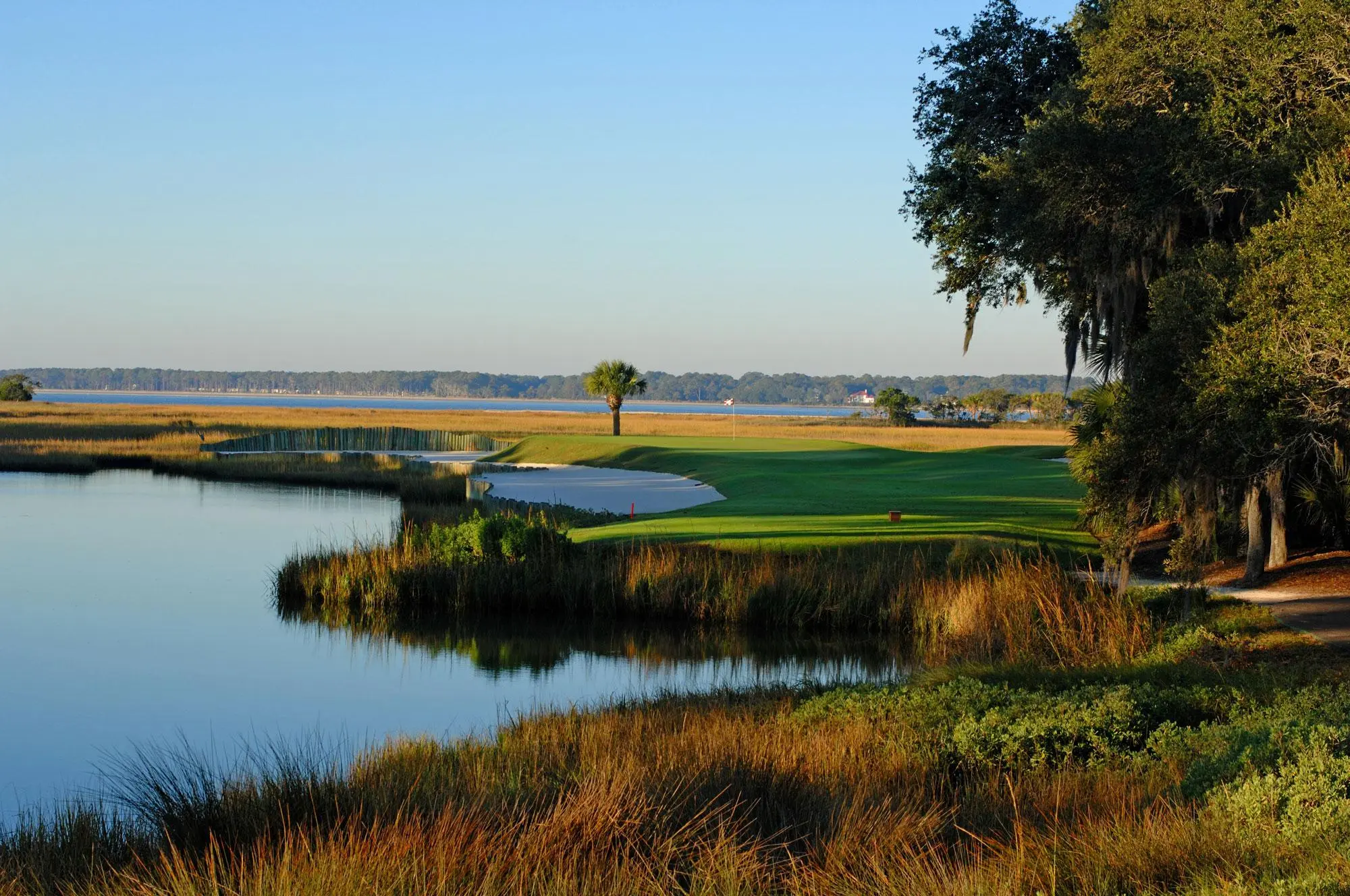 A peaceful golf hole surrounded by marsh grasses and calm waters.