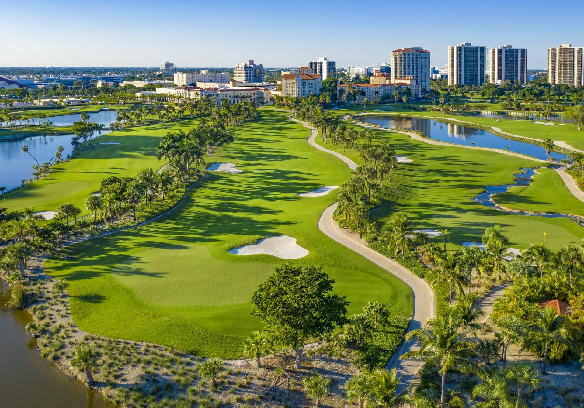 Panoramic aerial view of the course surrounded by palm trees and sand bunkers under clear blue skies