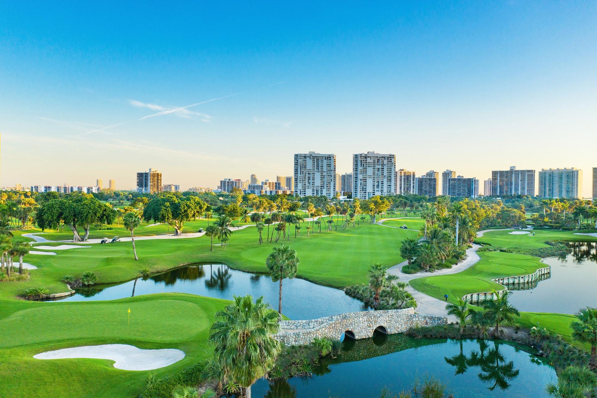 A vibrant golf course landscape with water features, stone bridges, and a backdrop of a bustling city skyline.