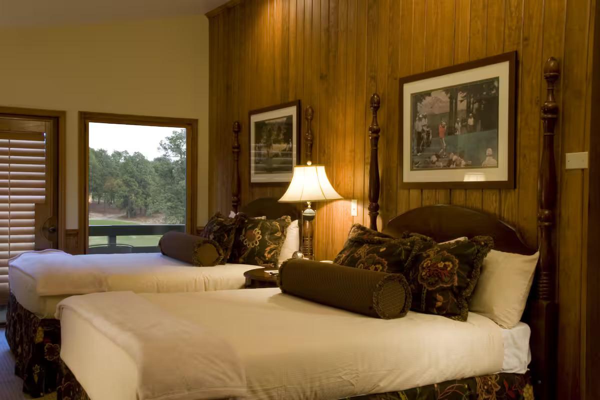 A rustic twin double bed room with golf related artwork hanging above the headboards and balcony views of the course