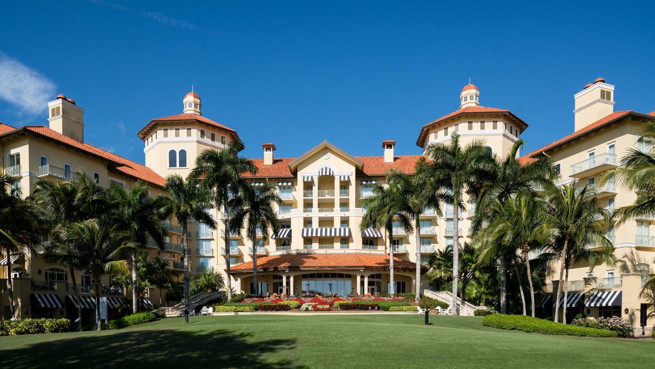 The Ritz Carlton Naples grand entrance with a front garden and palm trees under clear blue skies