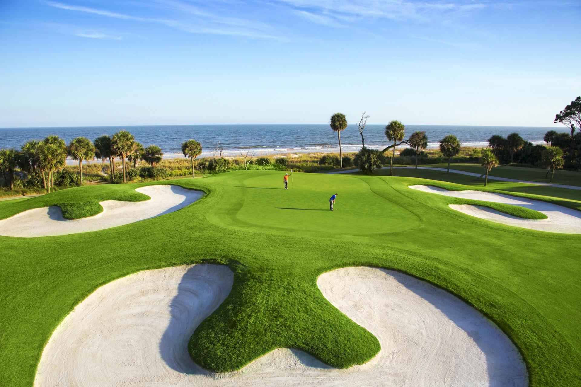 Golfers putting on a smooth green surrounded by uniquely shaped sand bunkers with sea views