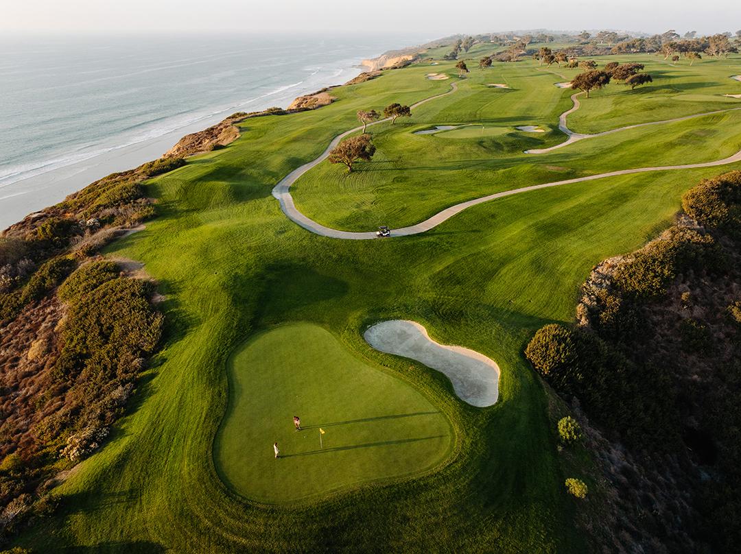 Aerial view of golfers enjoying their round on a smooth green with their buggy parked on the walkway