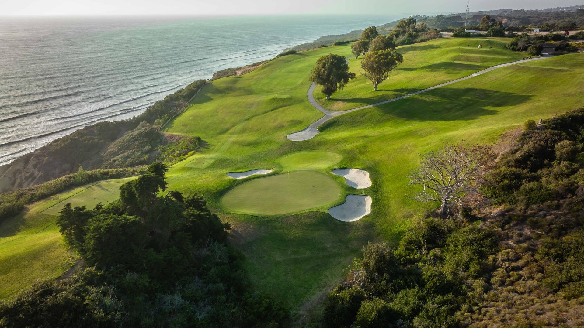 Overhead view of a smooth green surrounded by sand bunkers with sea views