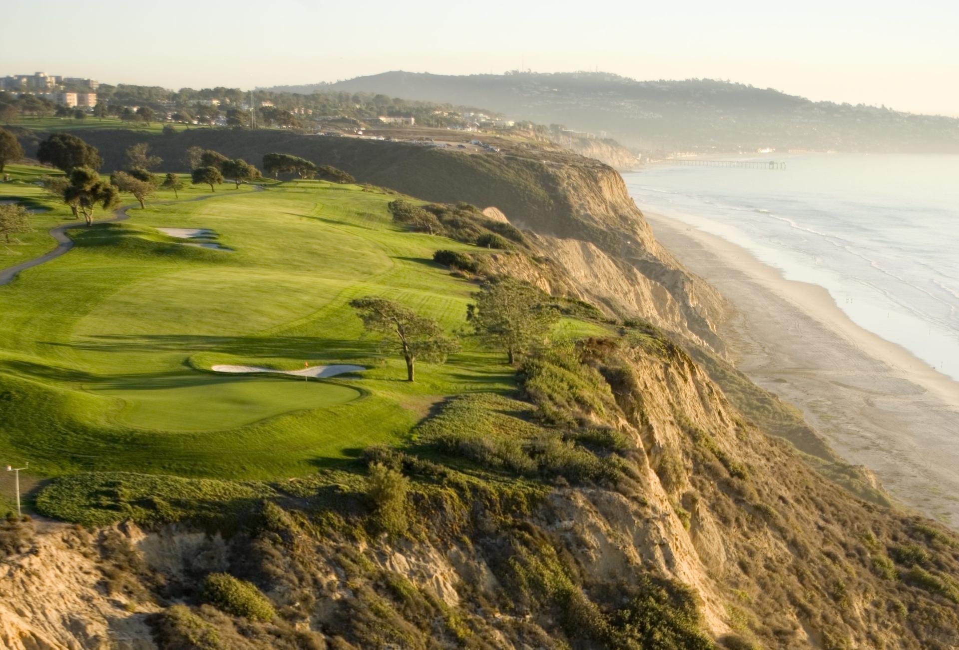 Panoramic view of a straight fairway leading to smooth green which runs down the coast