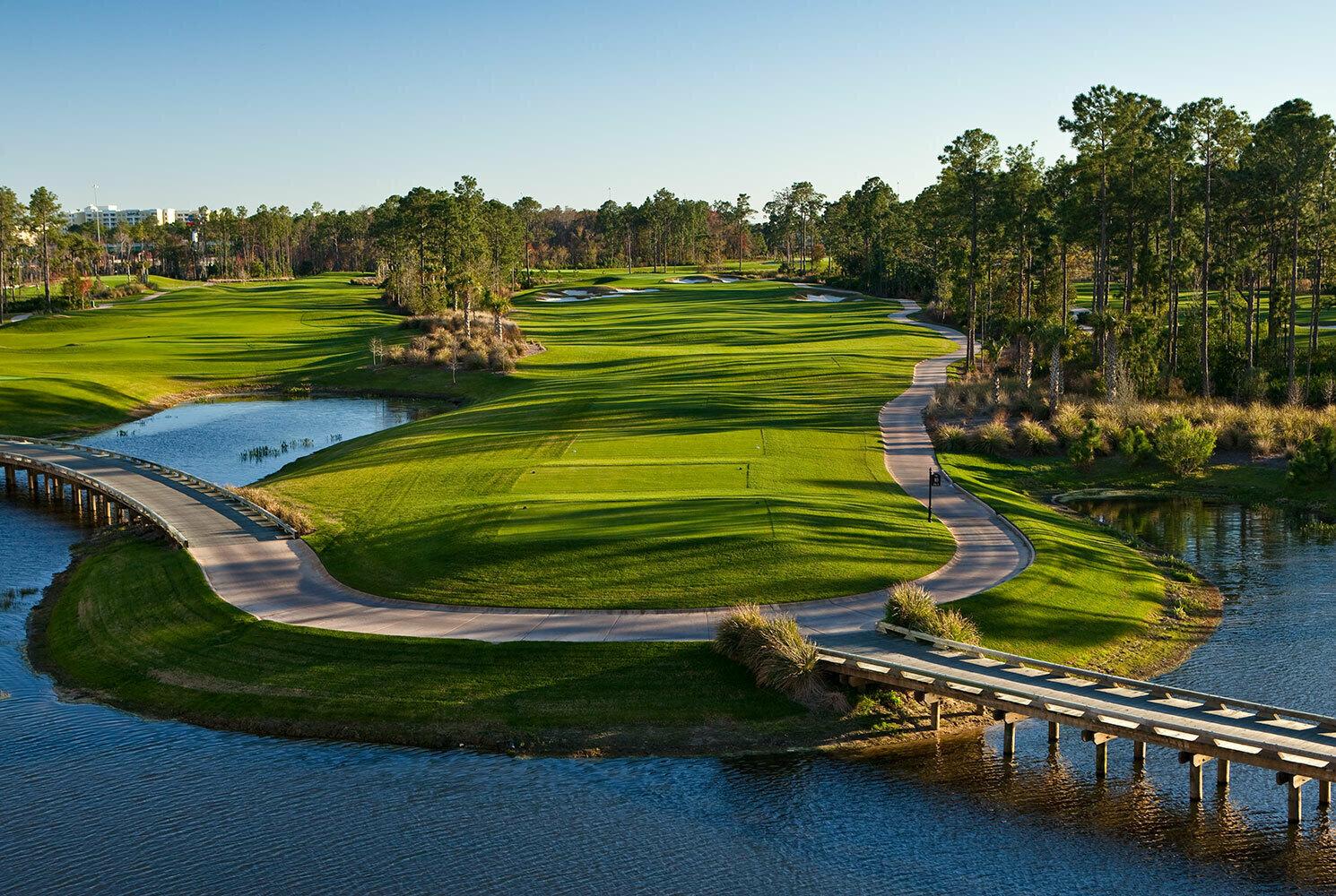 A winding golf course with bridges and water features surrounded by tall pines.
