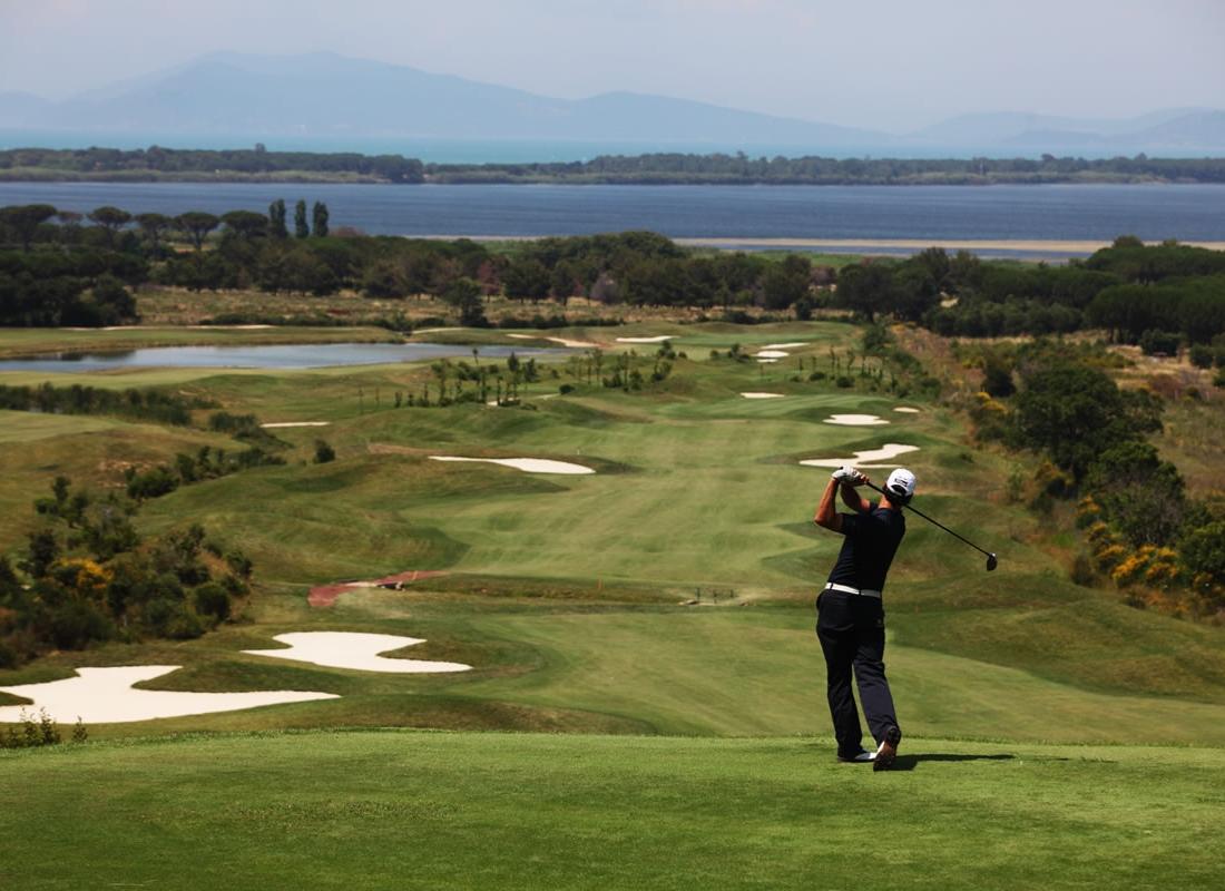 Golfer swinging towards a fairway littered with sand bunkers and sea views in the distance