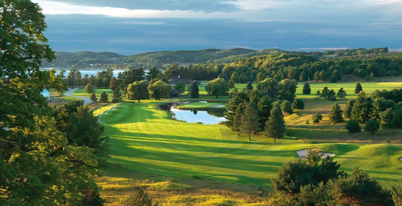 Tree-lined fairway leading to a reflective water hazard with lush hills in the background.