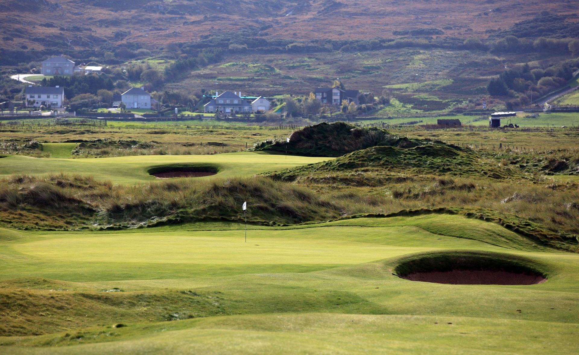 Close up view of a hole at the Ballyliffin course with surrounding bunkers and houses in the backgroud