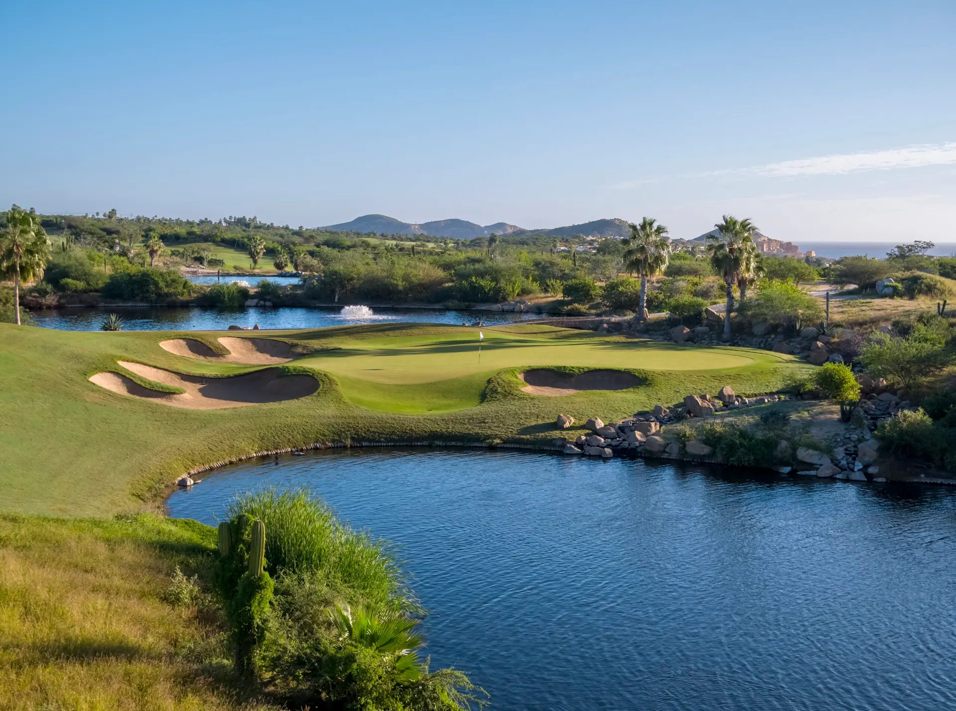 A manicured green surrounded by sand bunkers with mountain views in the distance