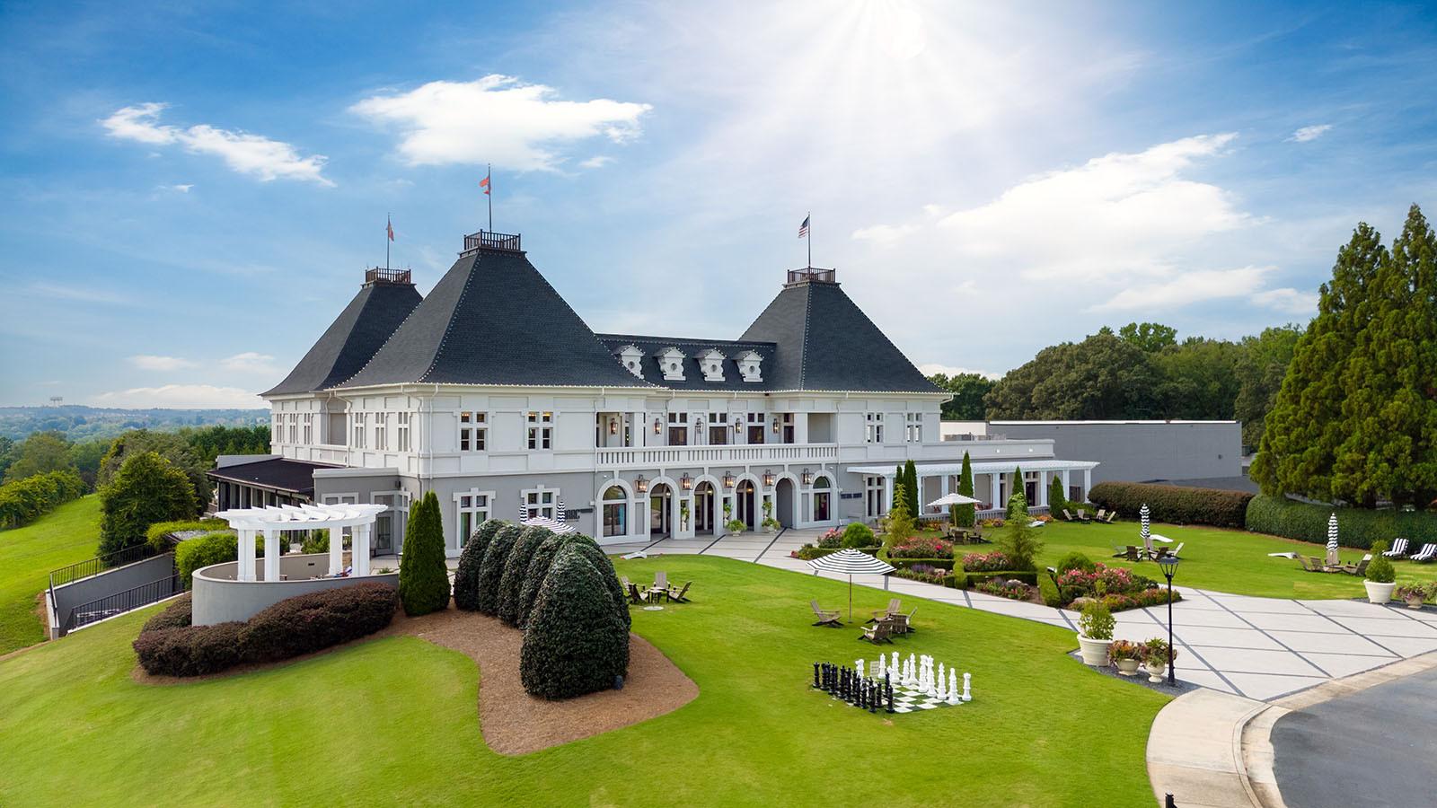 The resort’s French-inspired architecture stands proudly amidst lush green lawns and vibrant gardens under a bright blue sky.