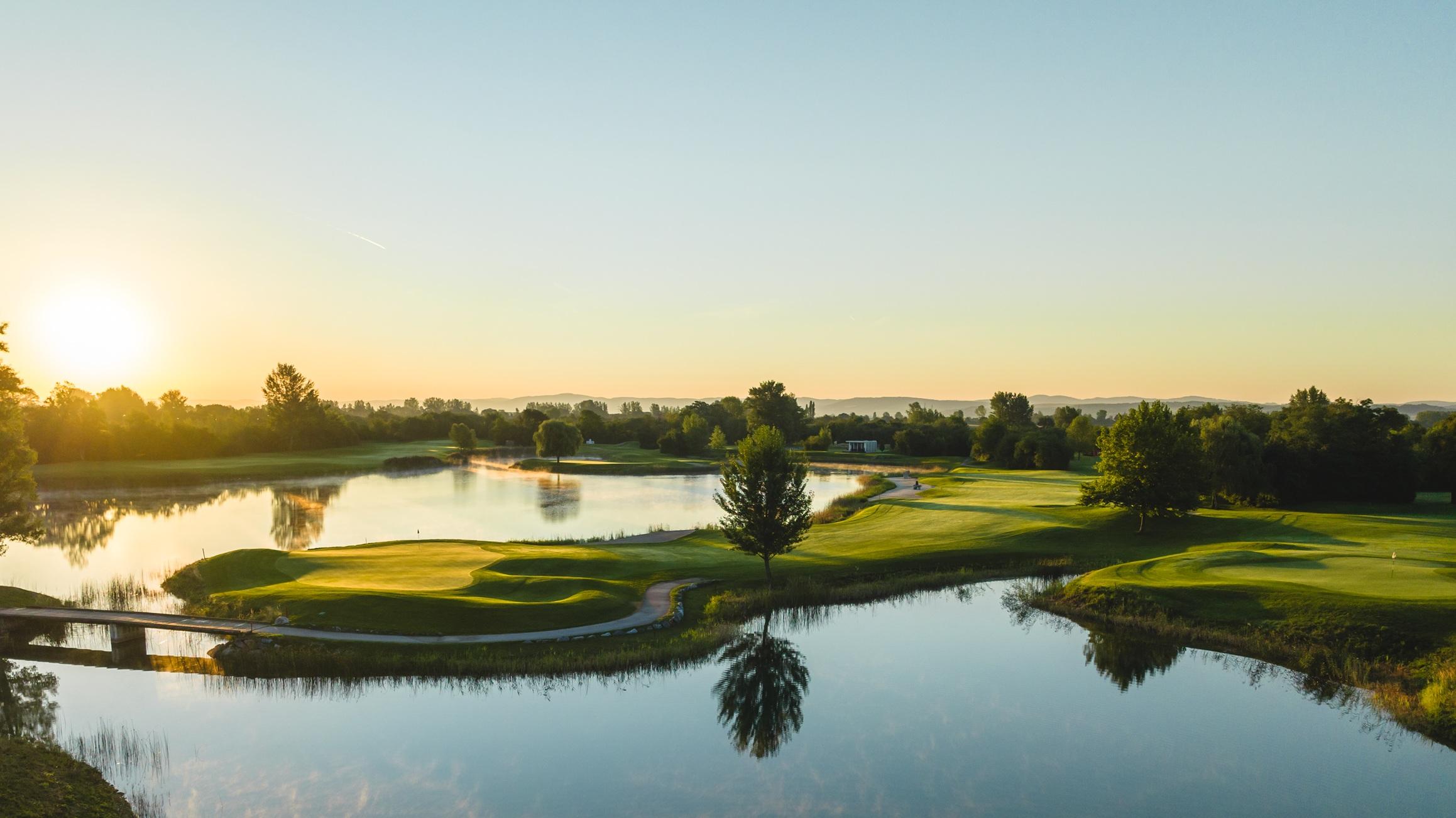 Sun setting over an island like green with a well-maintained fairway leading to it