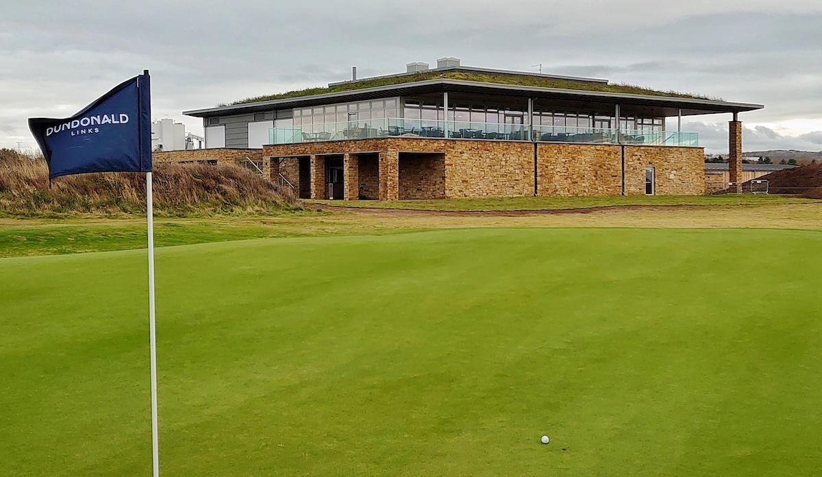 Branded flagstick swaying in the wind with its clubhouse building in the background