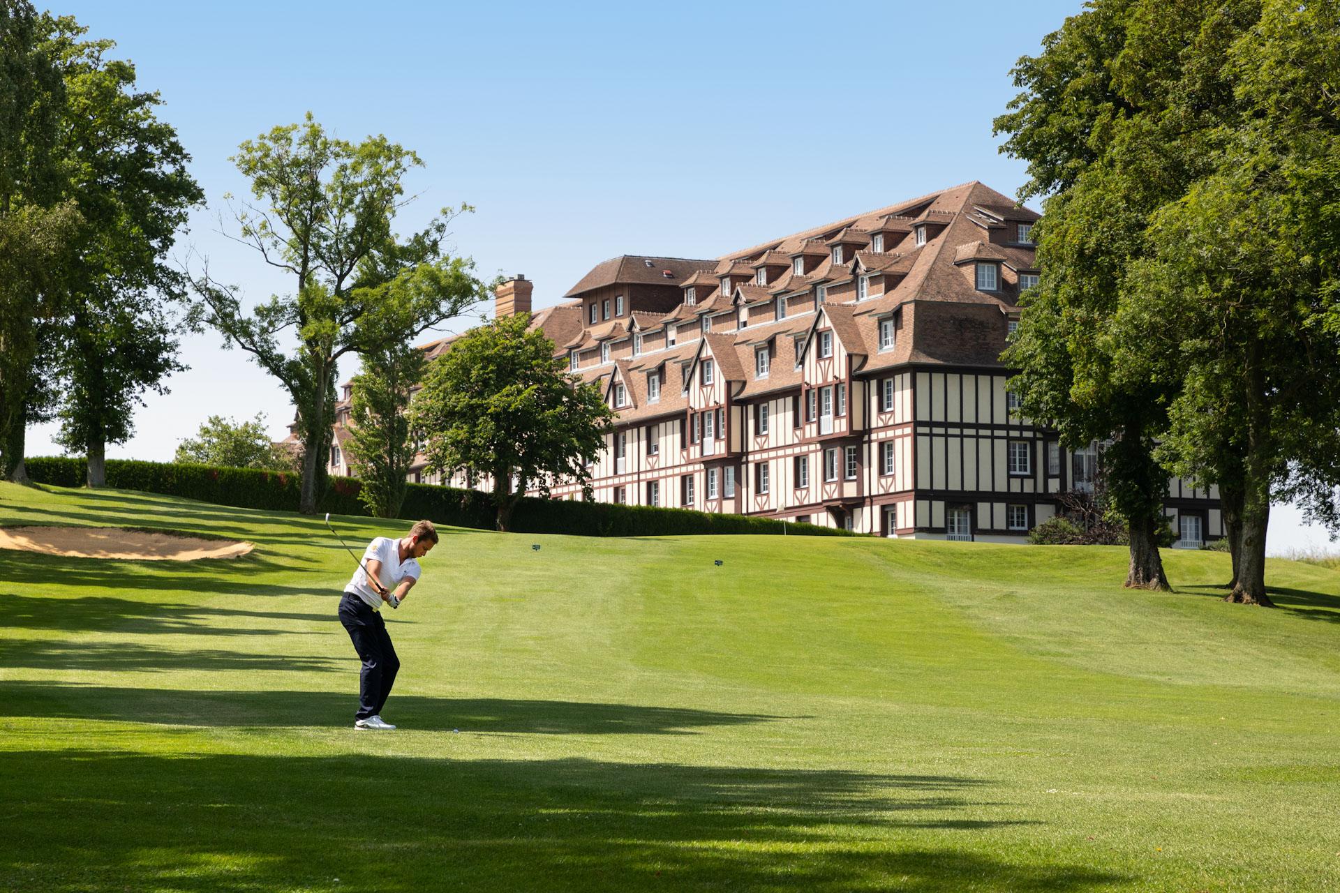 Player playing an up hill approach shot to the green with the Hotel Golf Barriere de Deauville in the background