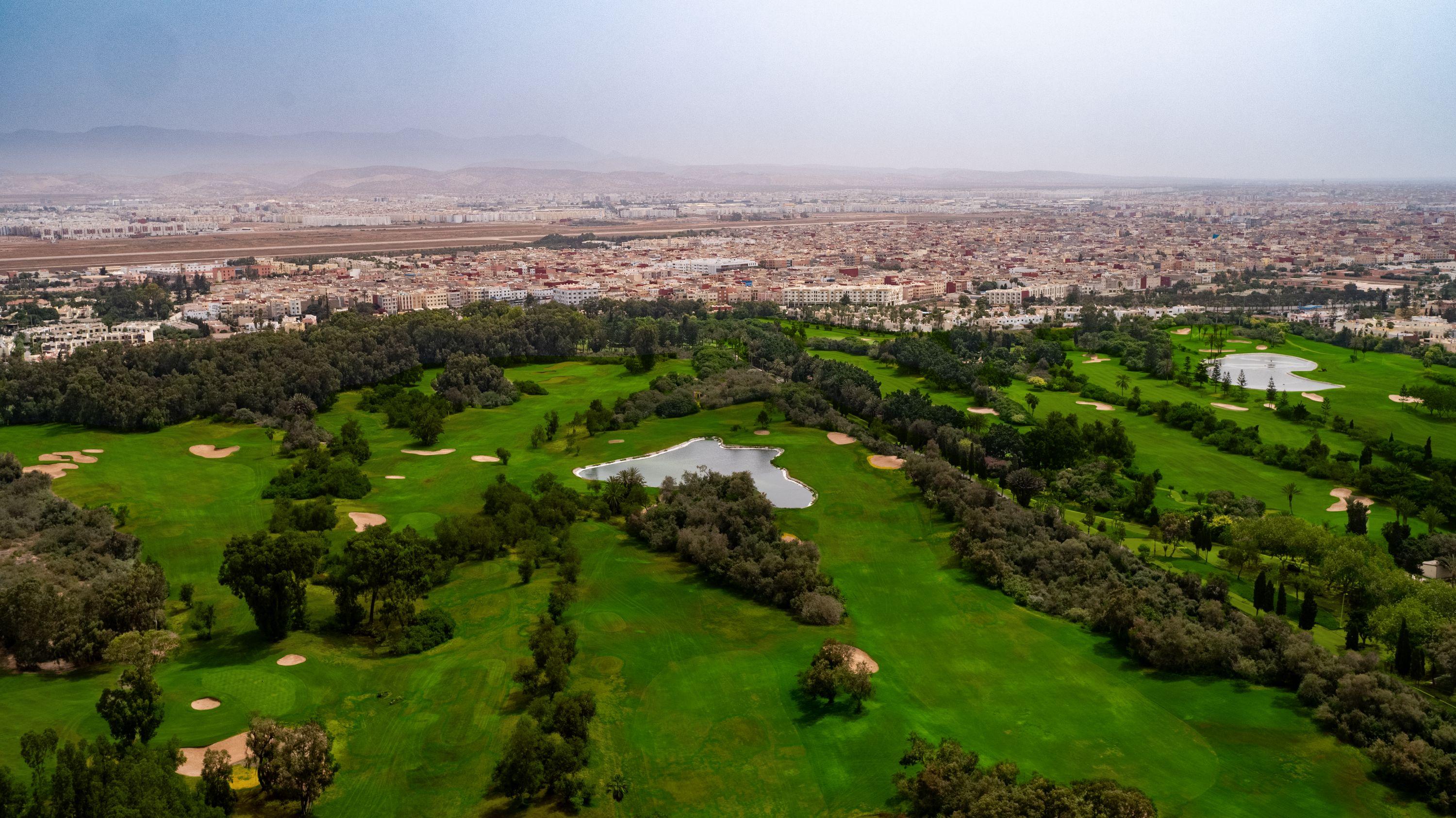 A sprawling golf course lies next to a bustling cityscape.