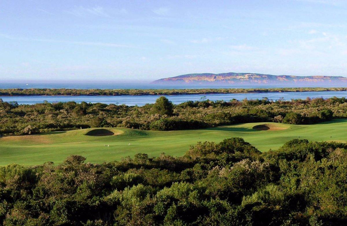 A lush green fairway stretching towards a blue river and distant cliffs.
