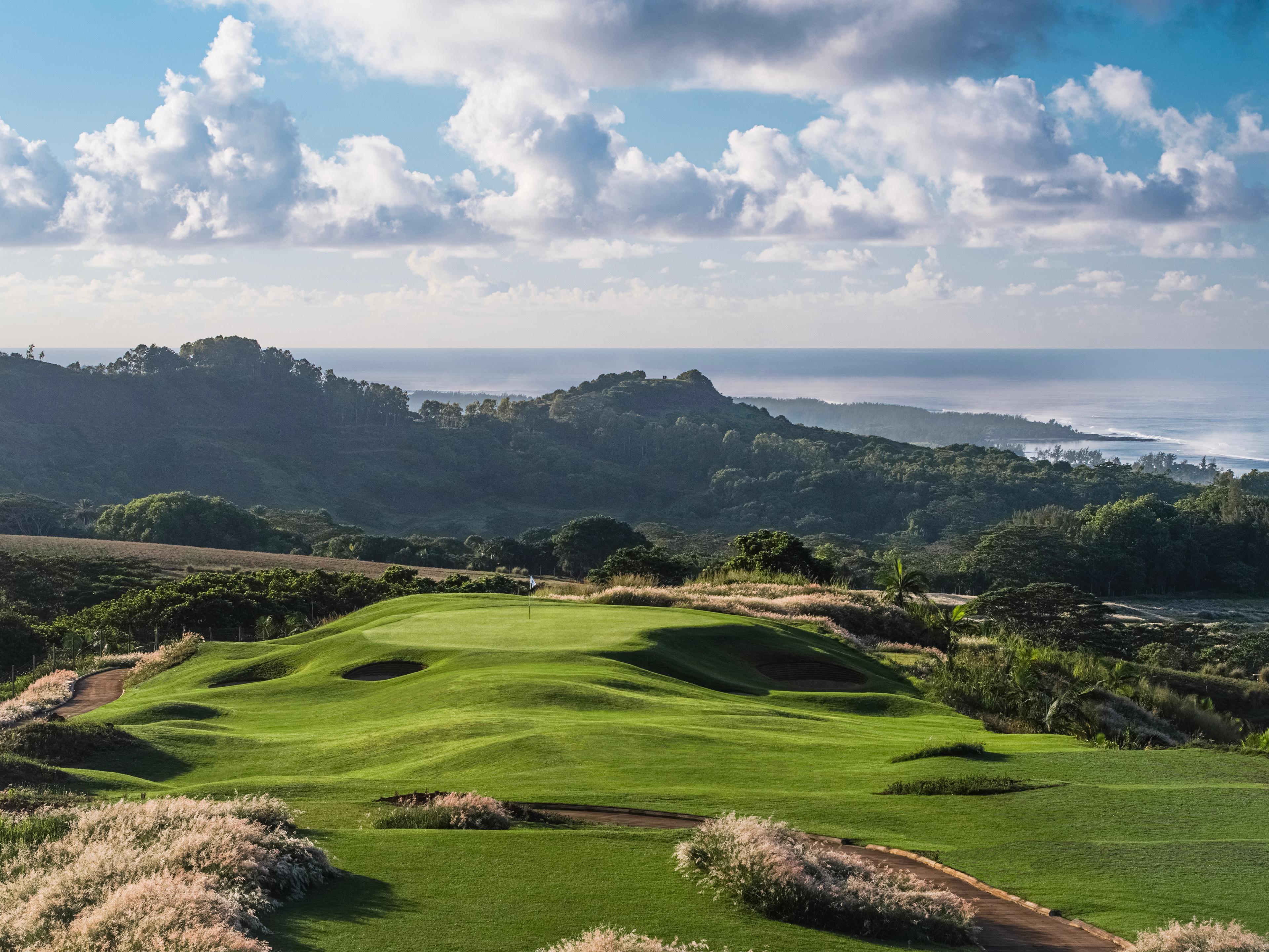 An elevated green surrounded by sand bunkers with coastal views