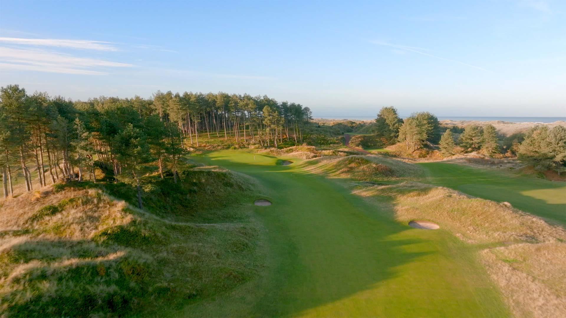 Overhead view of the fairway nestled with bunkers leading to the green with sea views in the distance
