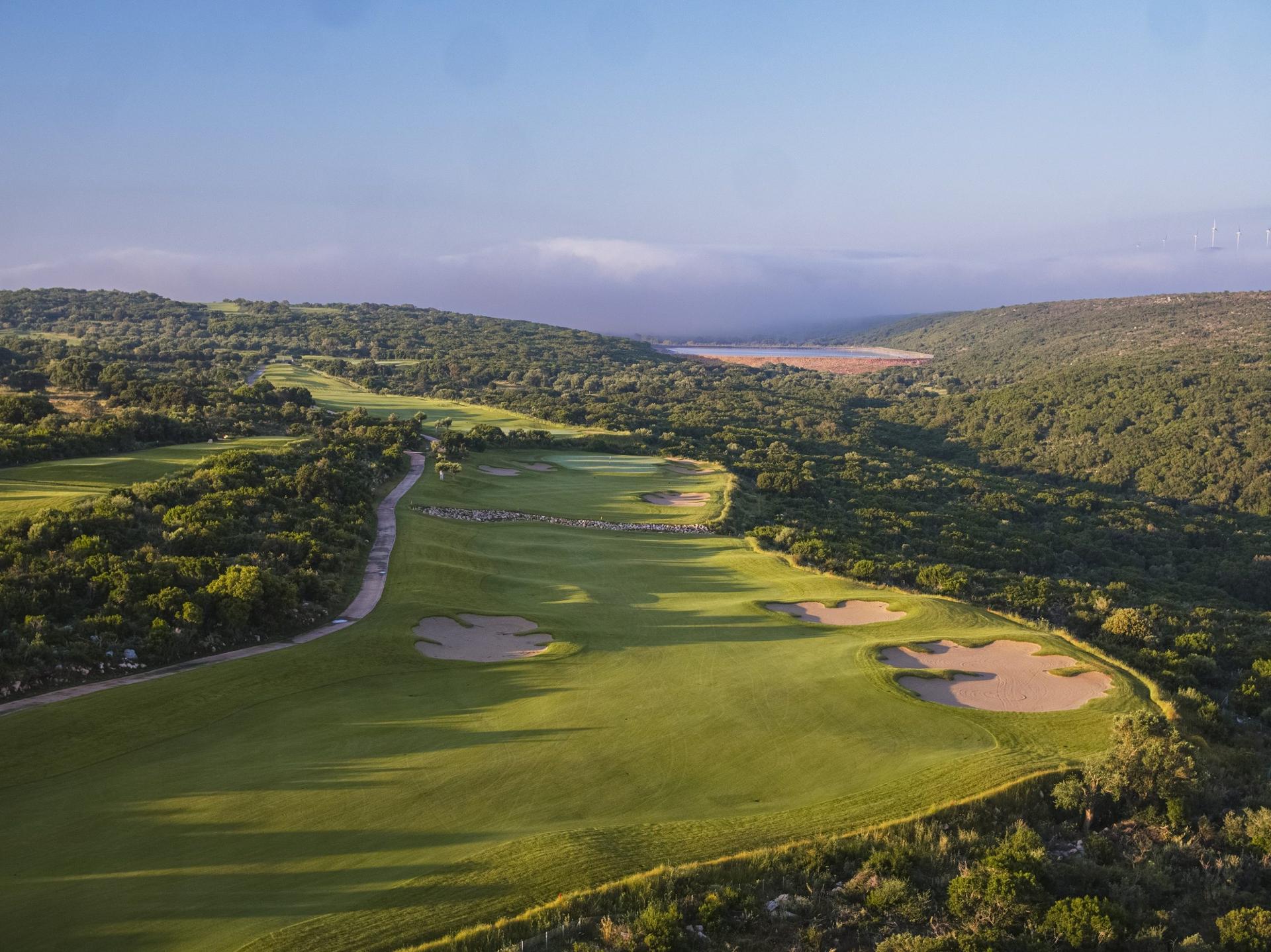 A wide fairway nestled with sand bunkers with a bushy rough surrounding