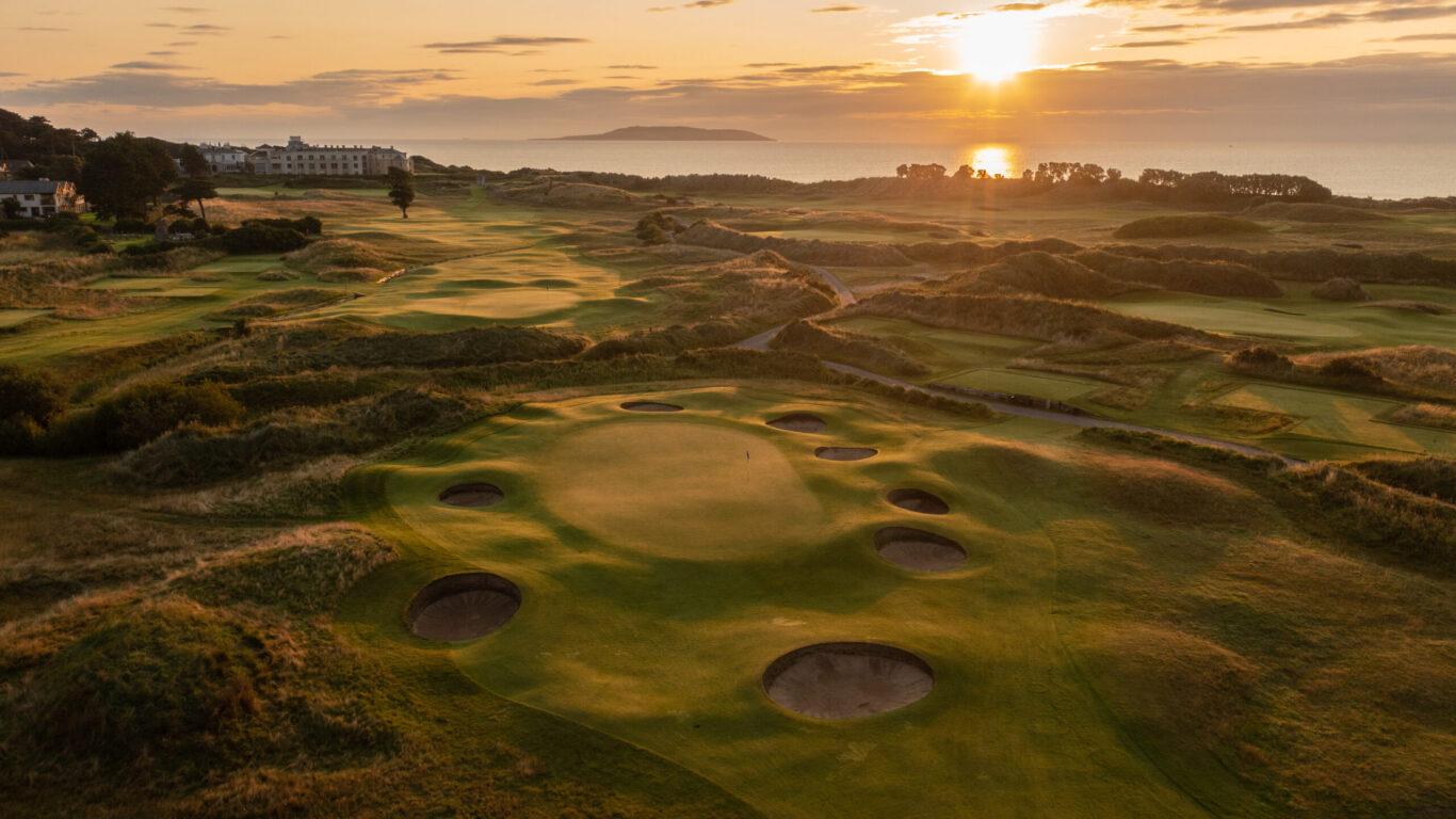 A scenic sunset view over a challenging golf green surrounded by bunkers.