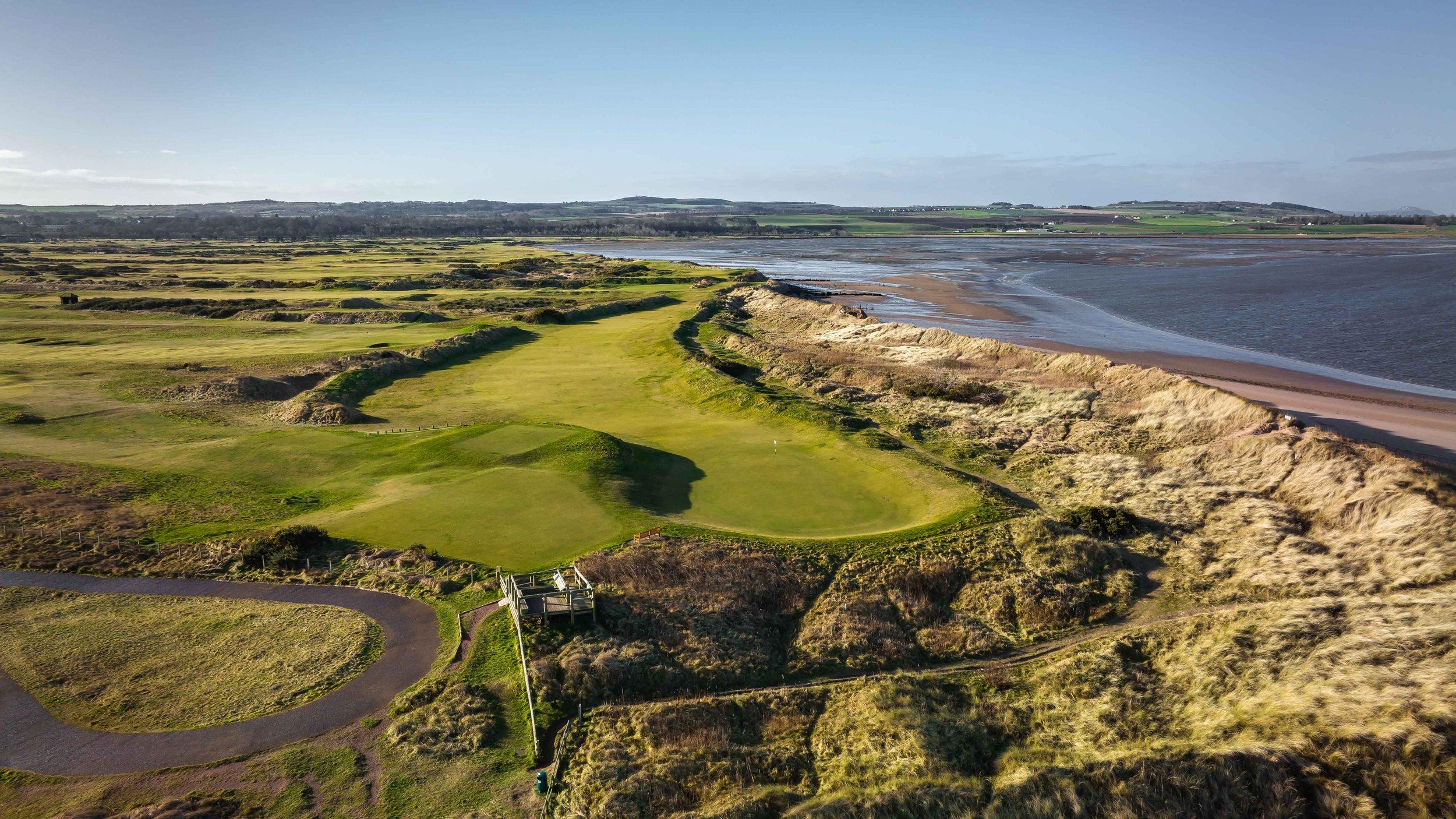 A sweeping fairway running along a sandy beach with waves crashing nearby.