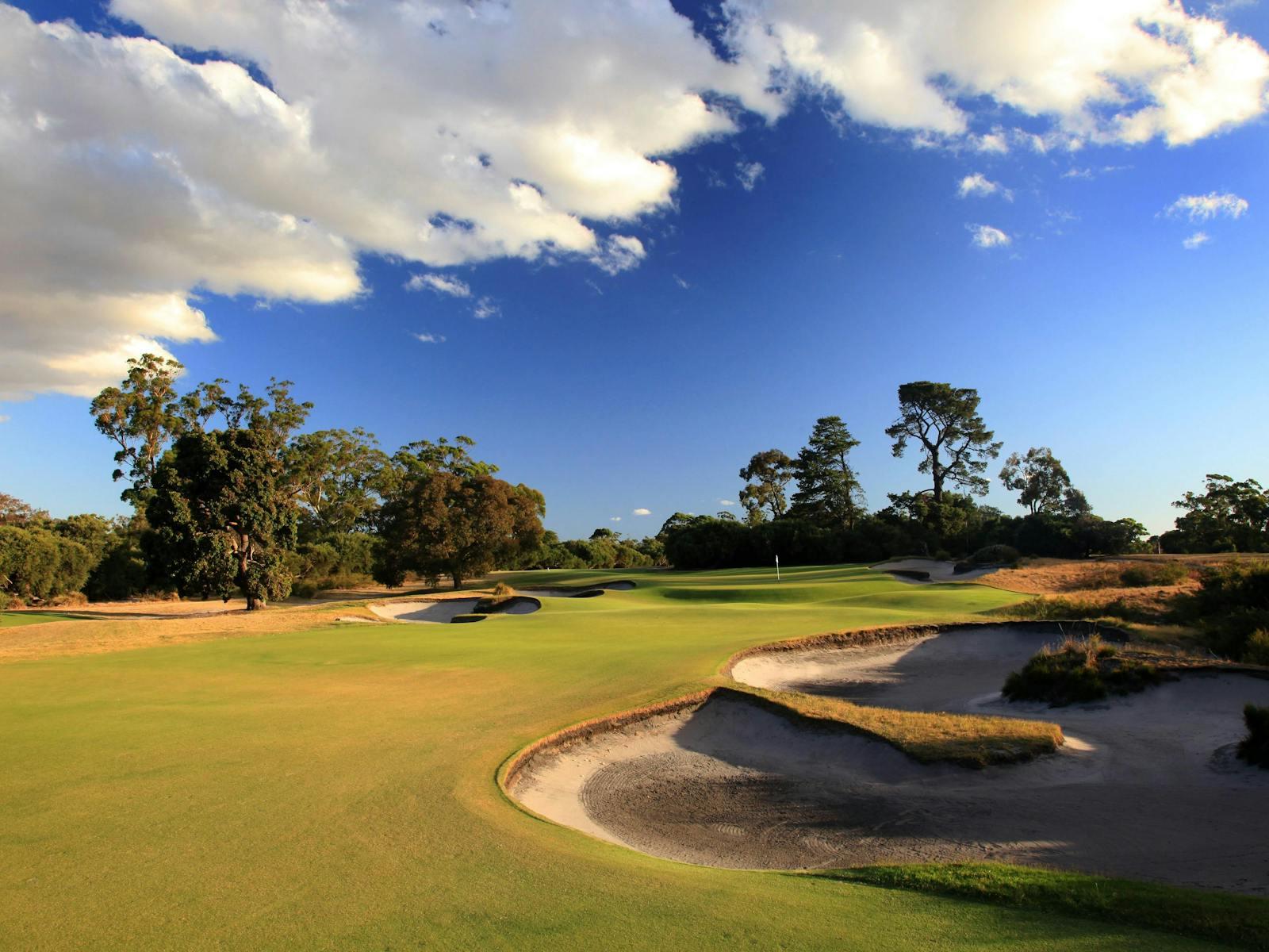 A smooth green surrounded sand bunkers under blue cloudy skies