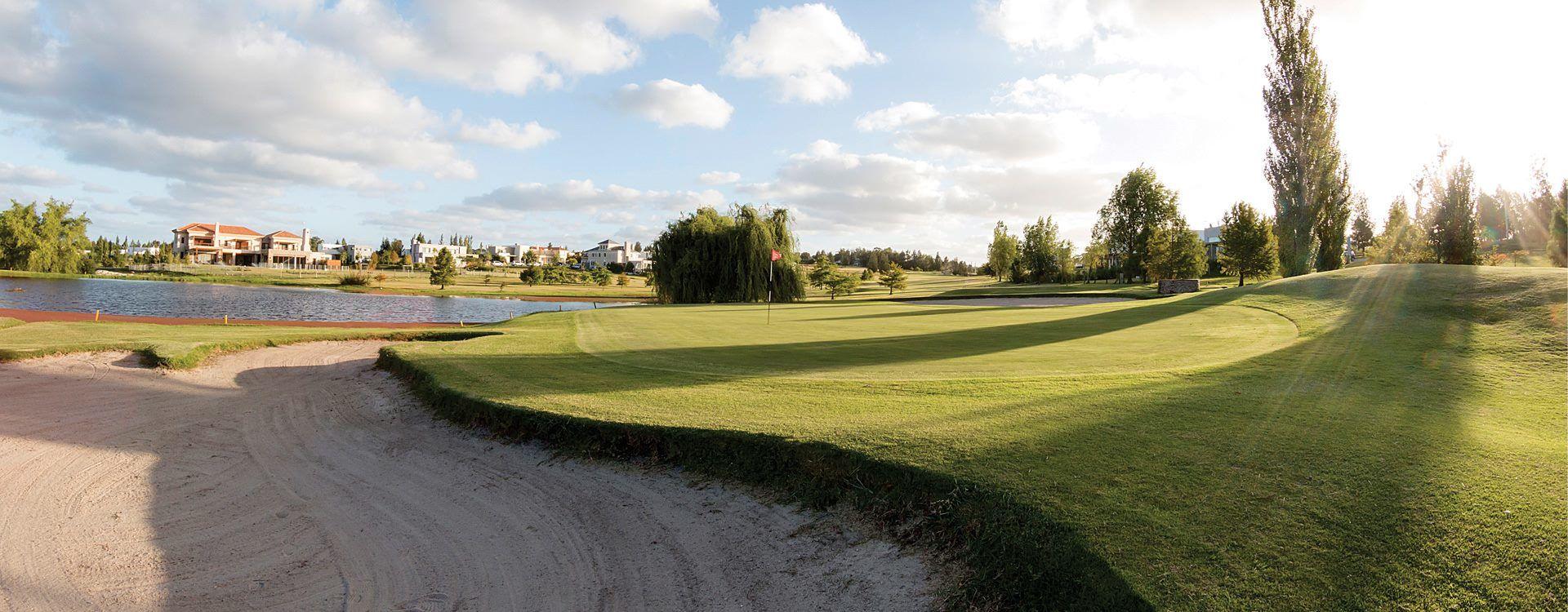 Sun shining over a smooth green surrounded by a sand bunker and water hazard