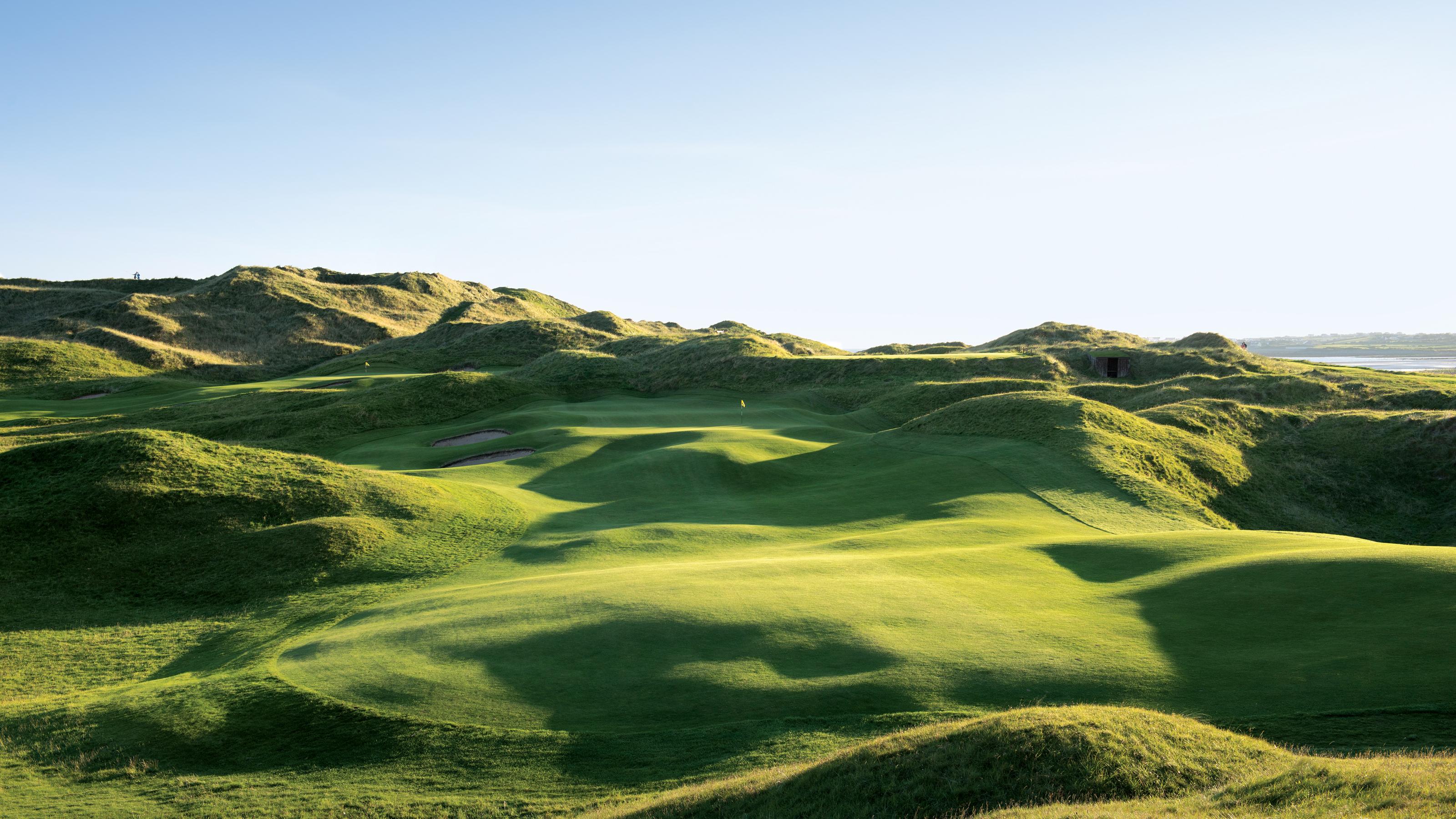 A lush, undulating fairway framed by dramatic dunes under a clear sky.