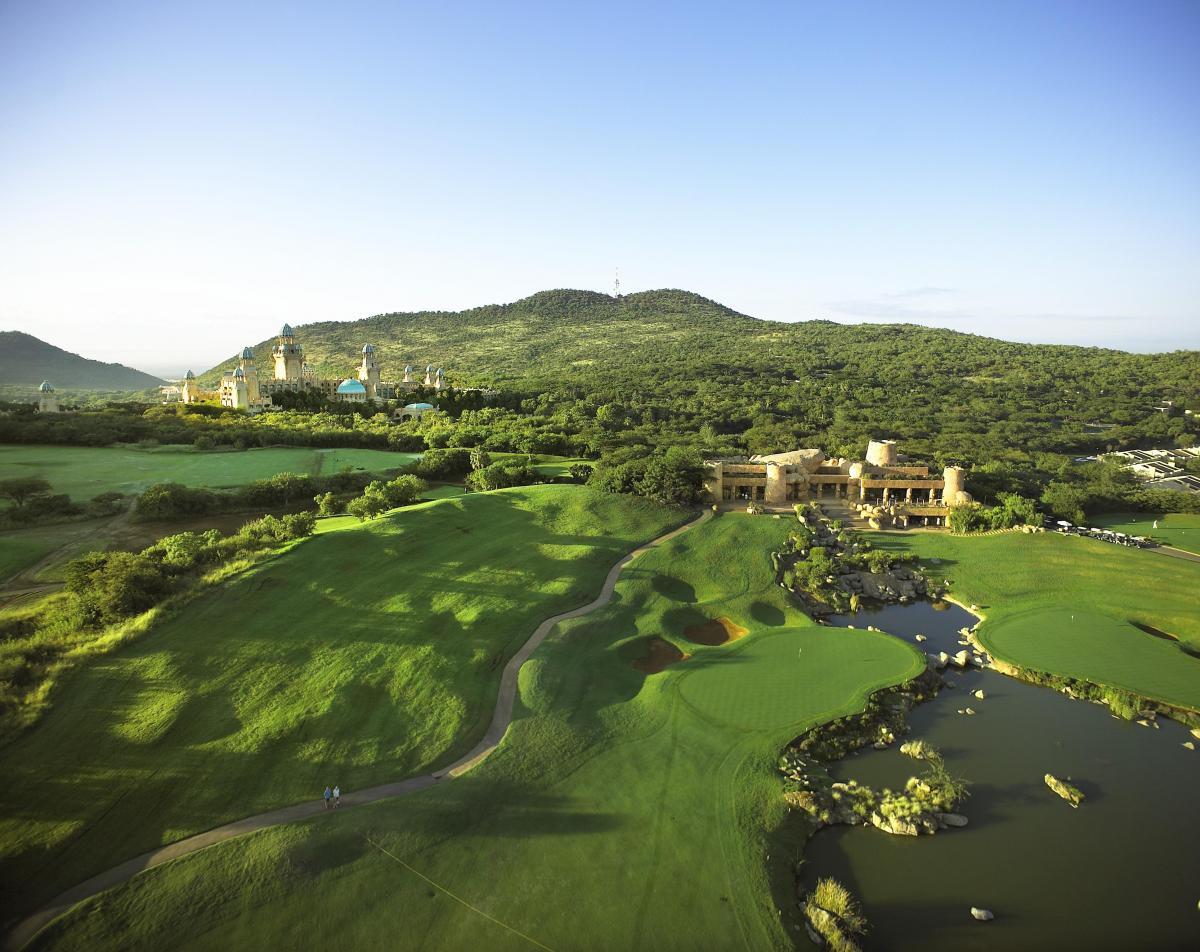 A wide aerial view of the golf course nestled between forests and mountains.