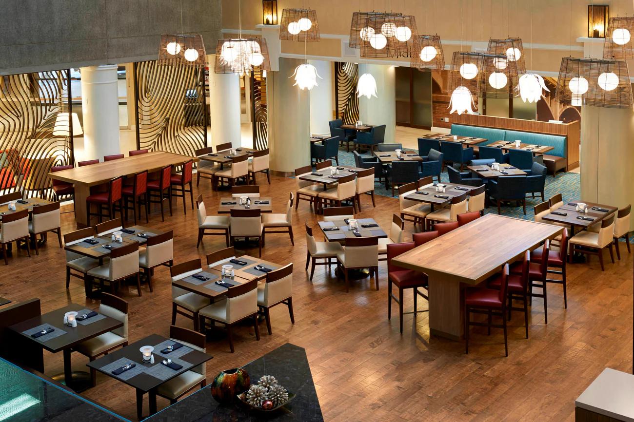 A contemporary hotel restaurant with wooden floors, stylish lighting, and neatly arranged tables.