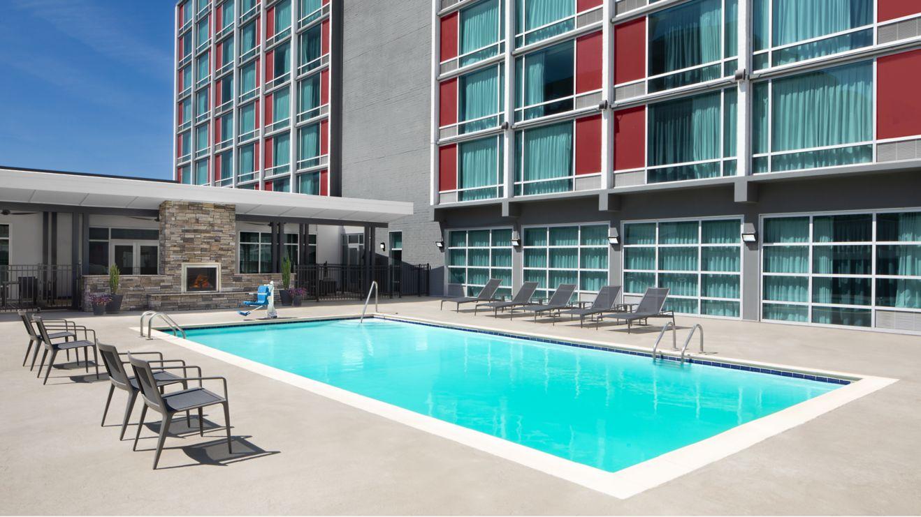 An outdoor hotel pool surrounded by lounge chairs and a fireplace feature.