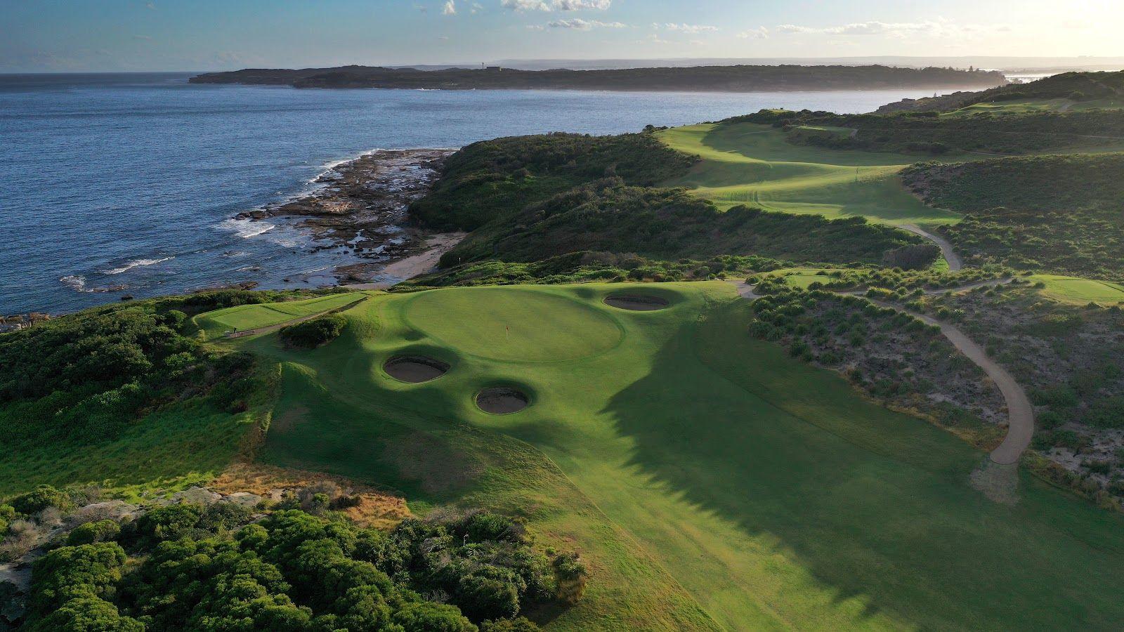 Birdseye view of a manicured elevated green surrounded by sand bunkers with coastal views