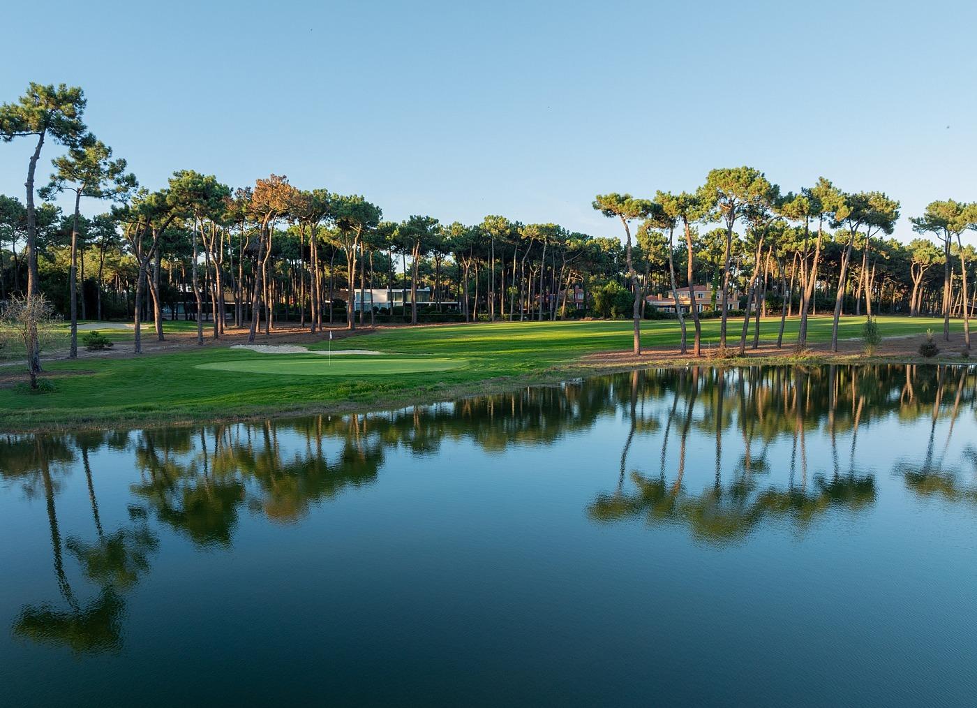 Tree-lined fairway at PGA Aroeira Lisbon leading to a green with water behind