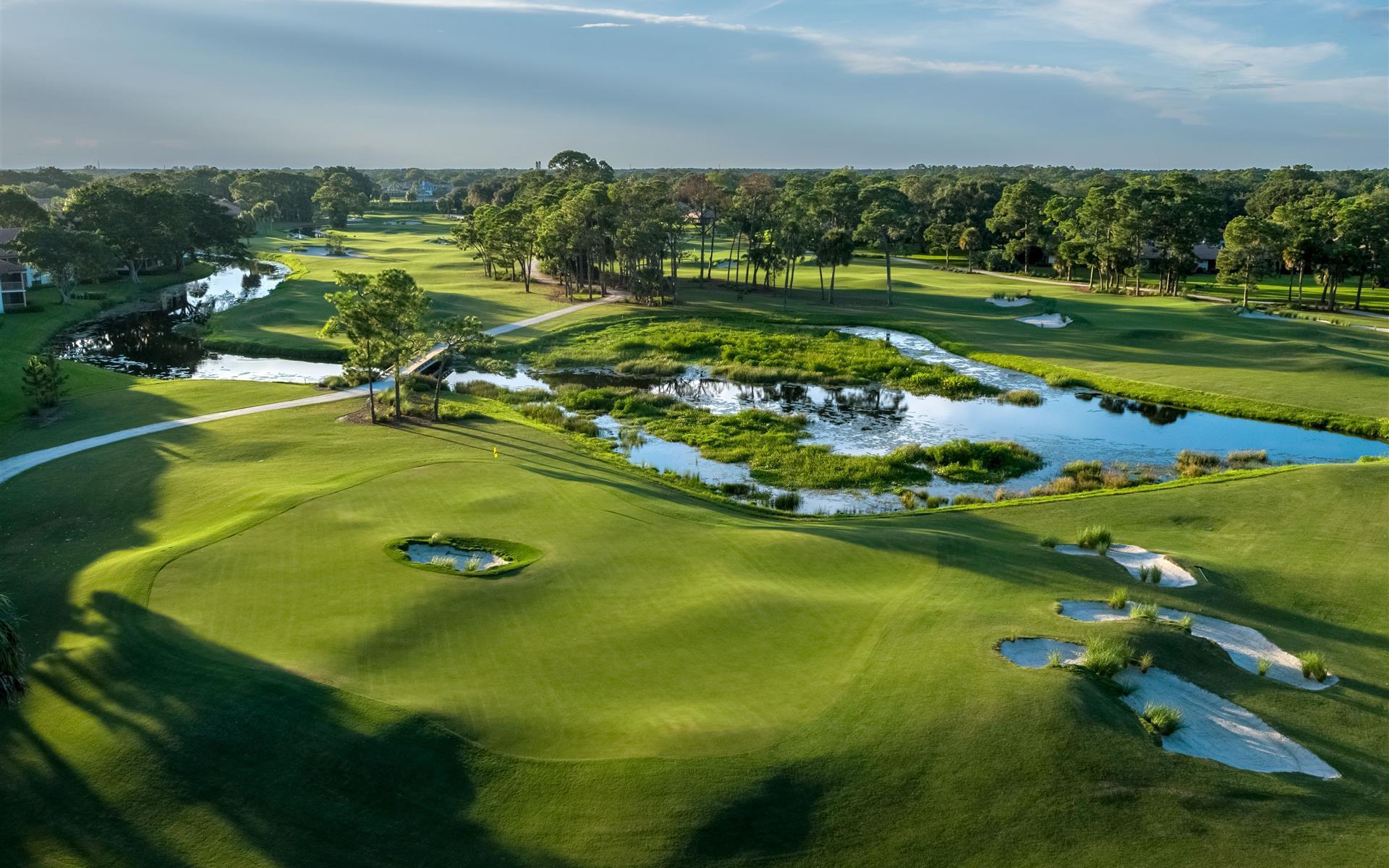 A lush golf course with water features and tree-lined fairways.