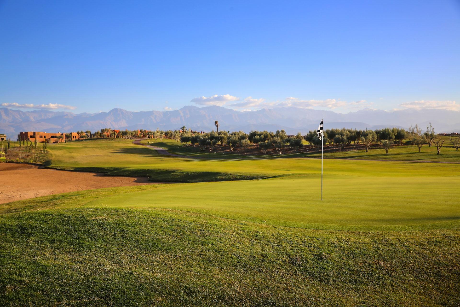 A smooth green next to a large sand bunker with distant mountain views