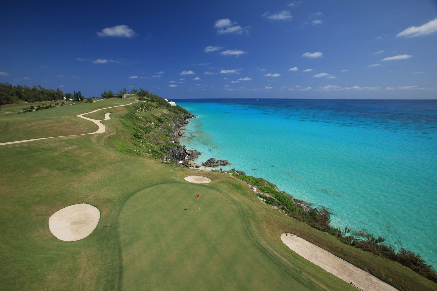 Overhead shot of a manicured green surrounded by sand bunkers next to the coast