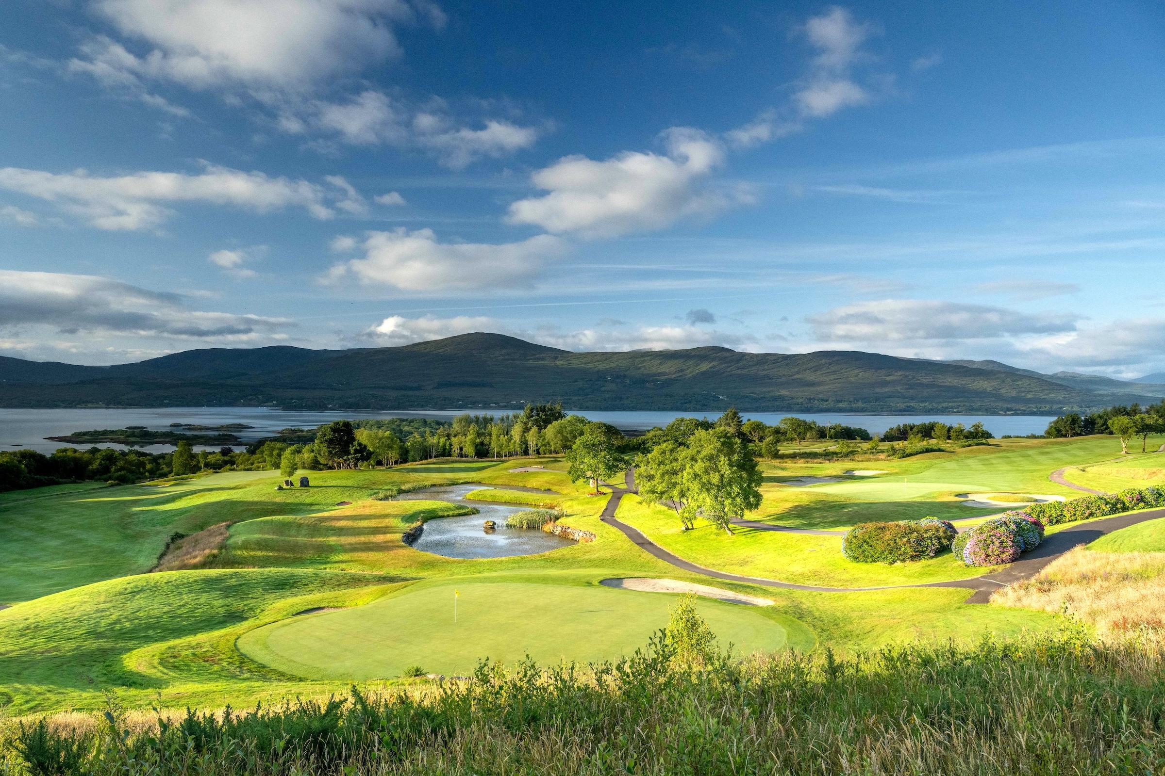 Picturesque fairways winding through lush landscape with ponds and mountain views.